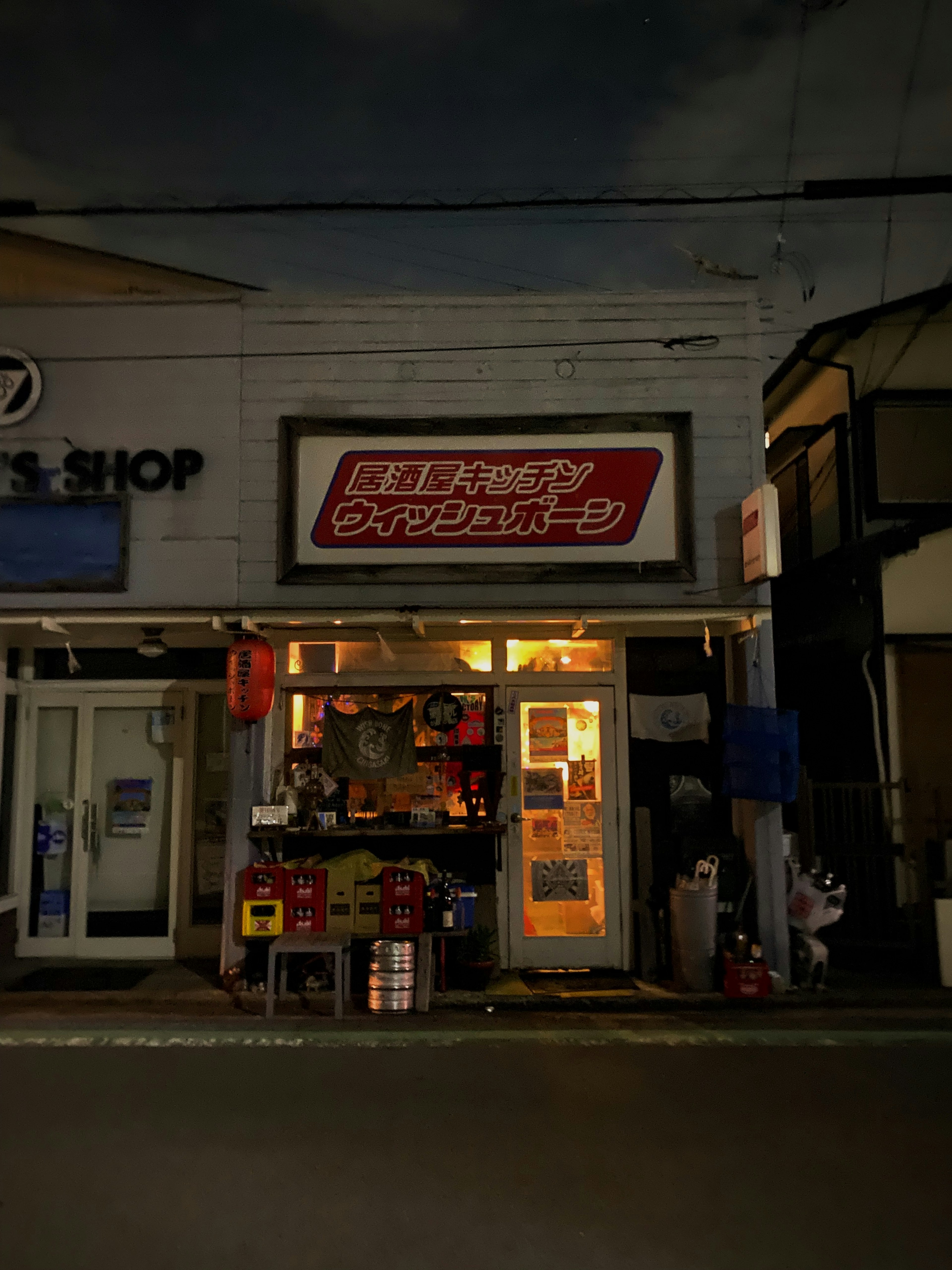 Exterior of a small shop in a nighttime street scene with Japanese signage