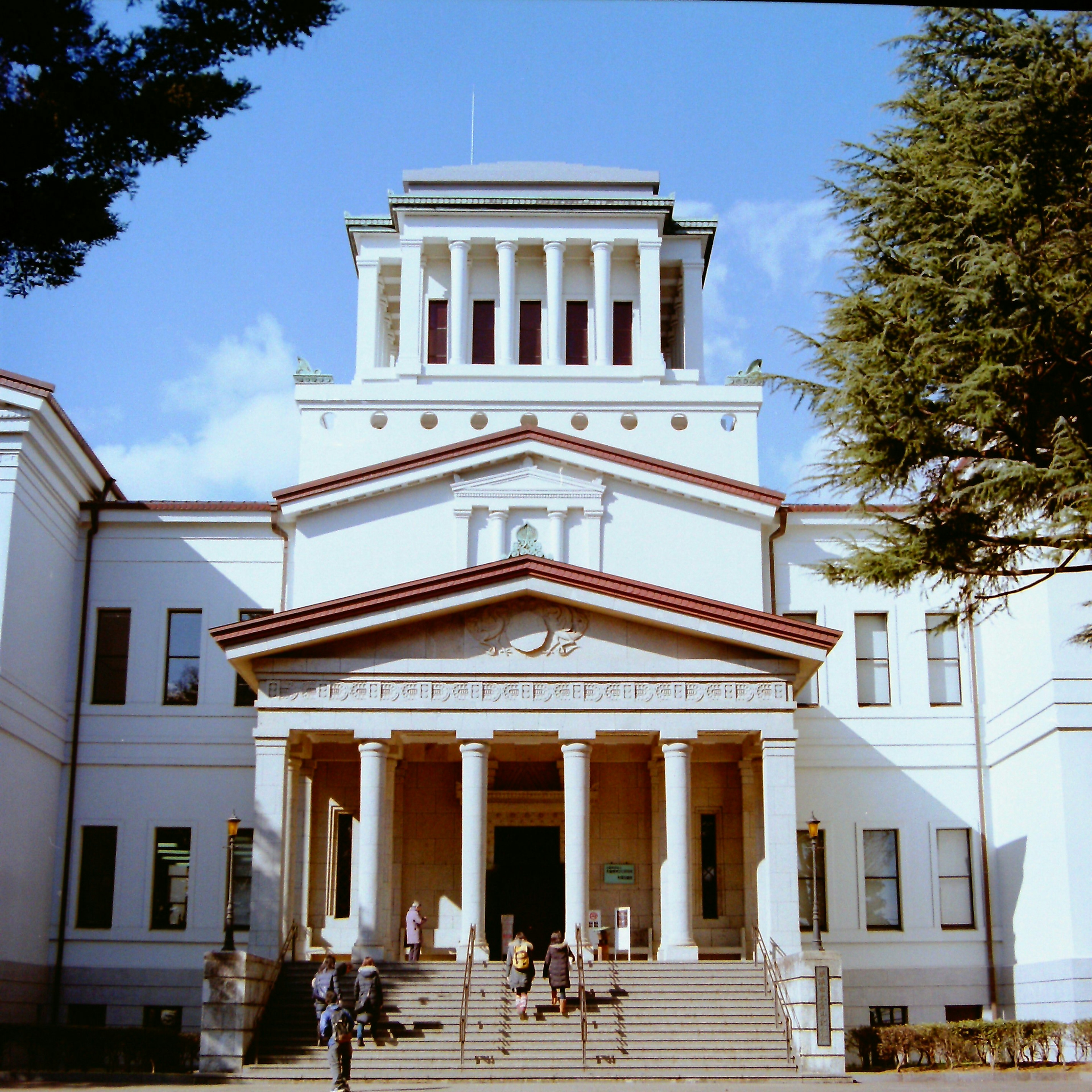 Historic building exterior with columns and stairs people under blue sky