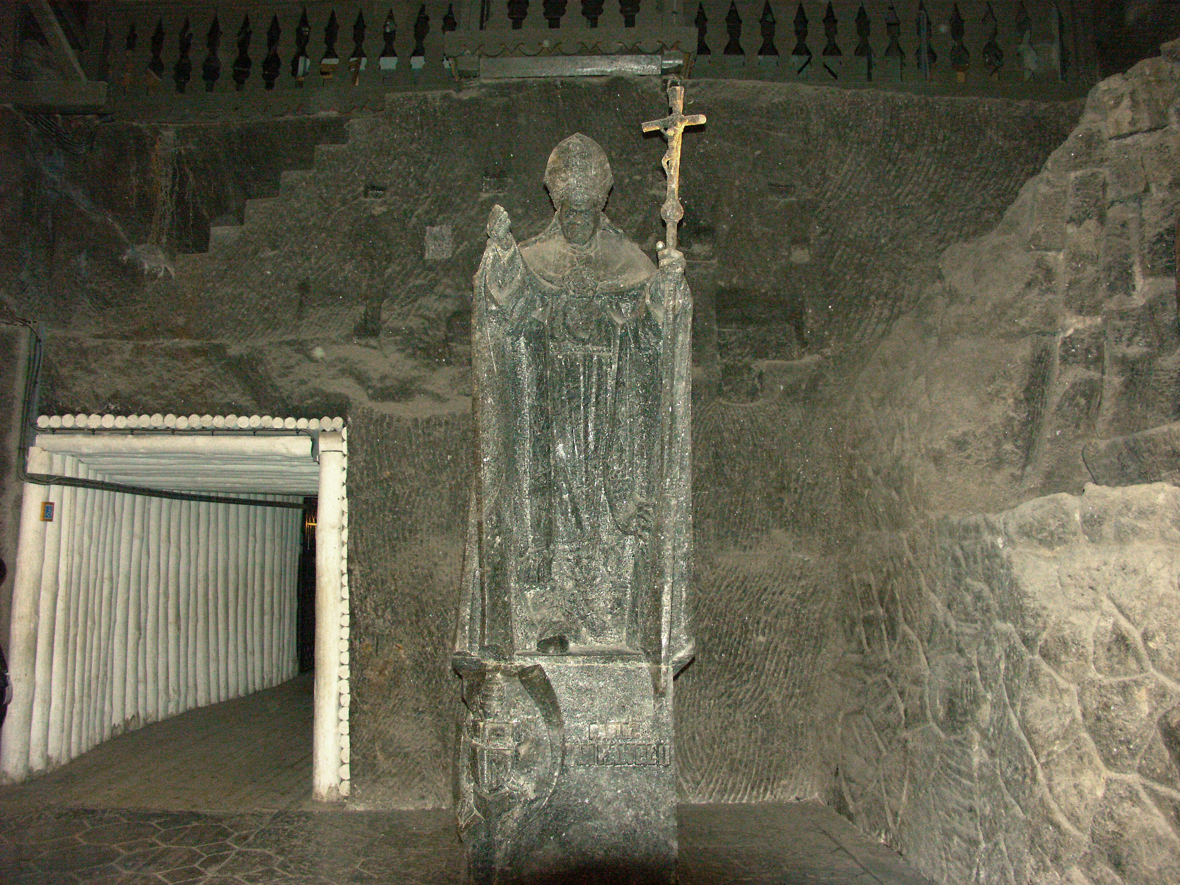 Statue en pierre d'un clerc tenant une croix dans un cadre souterrain