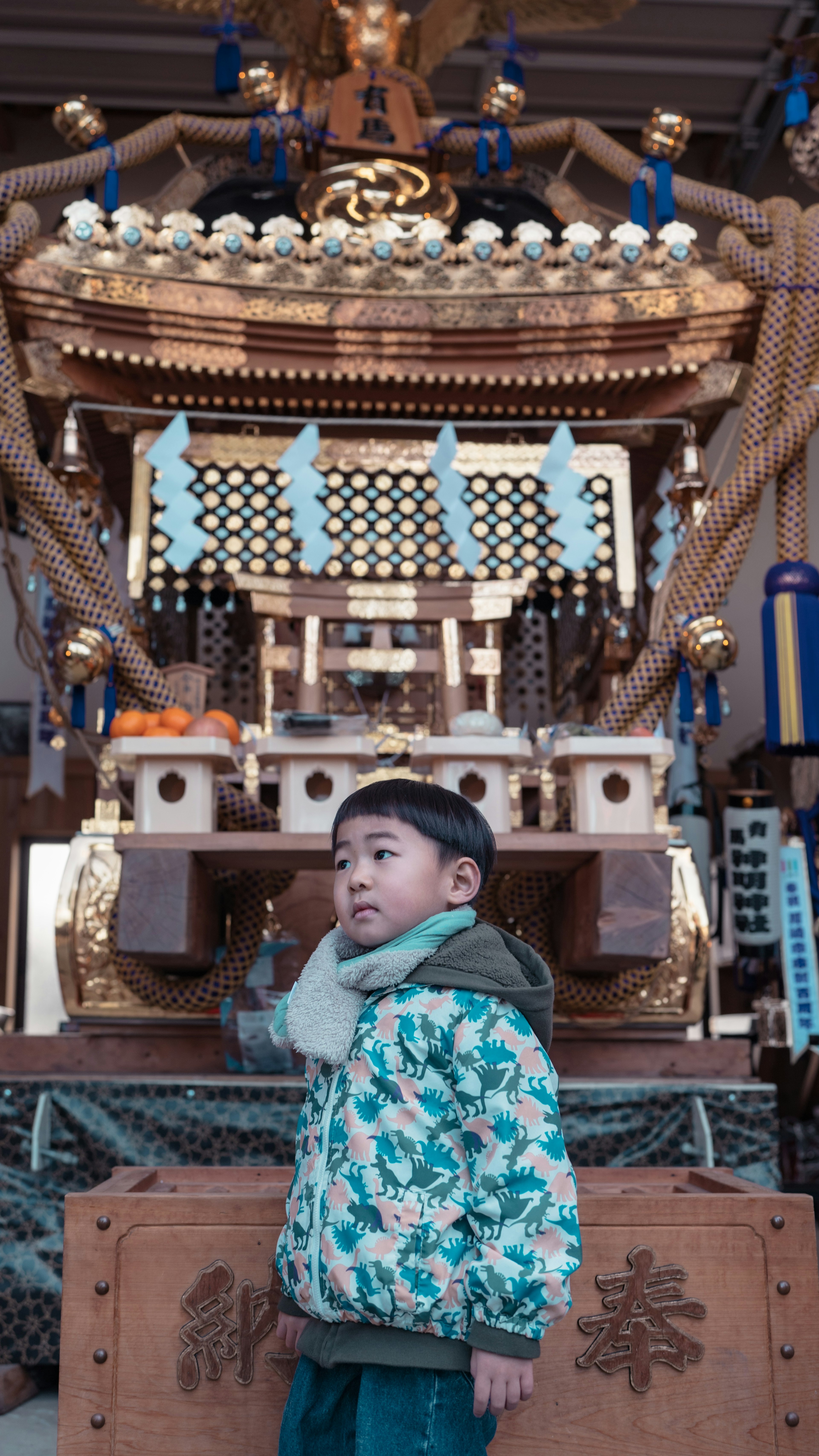 子供が神輿の前に立っている様子 神輿は金色で装飾されている