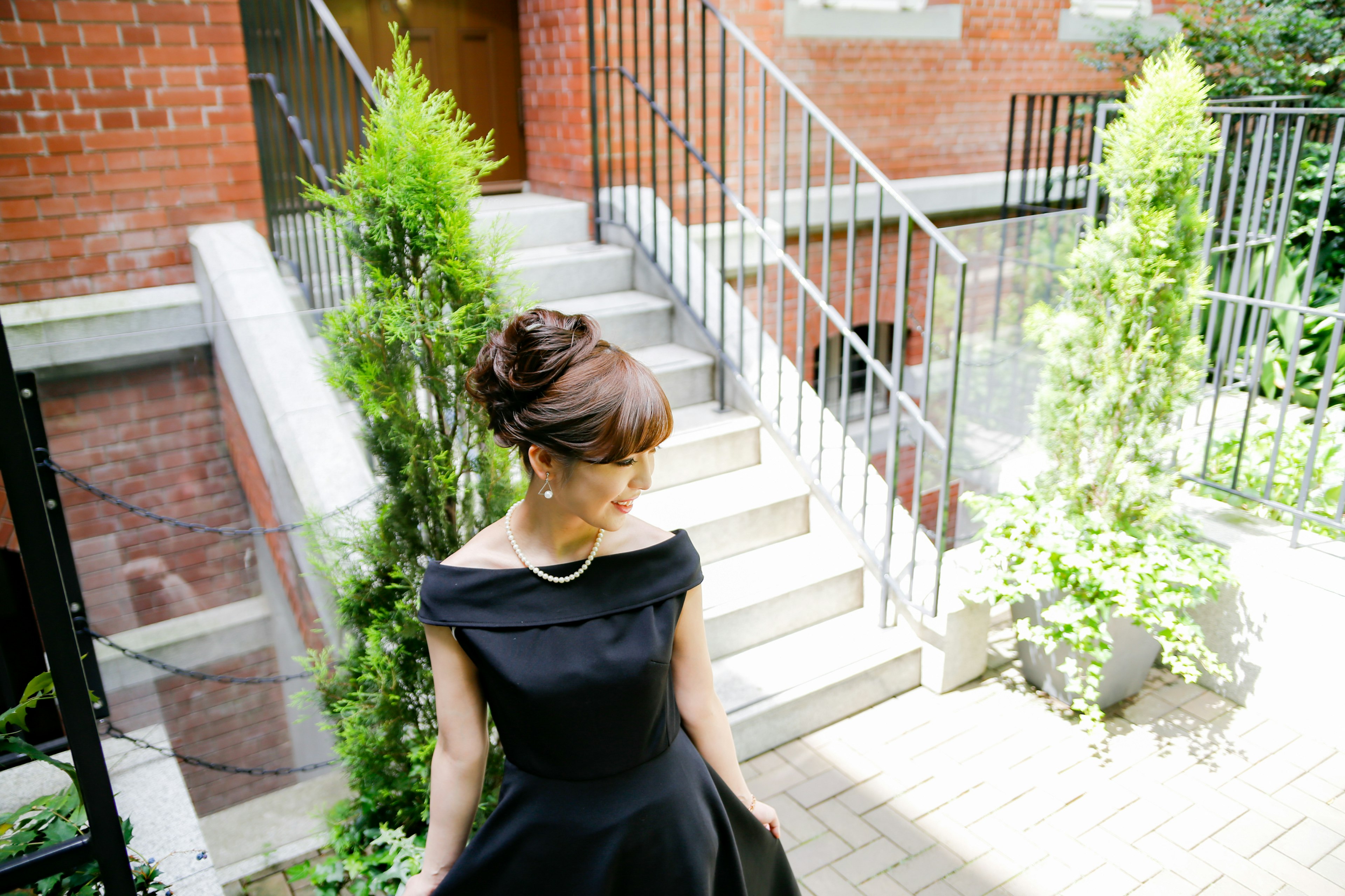 A woman in a black dress standing near stairs with greenery in soft light