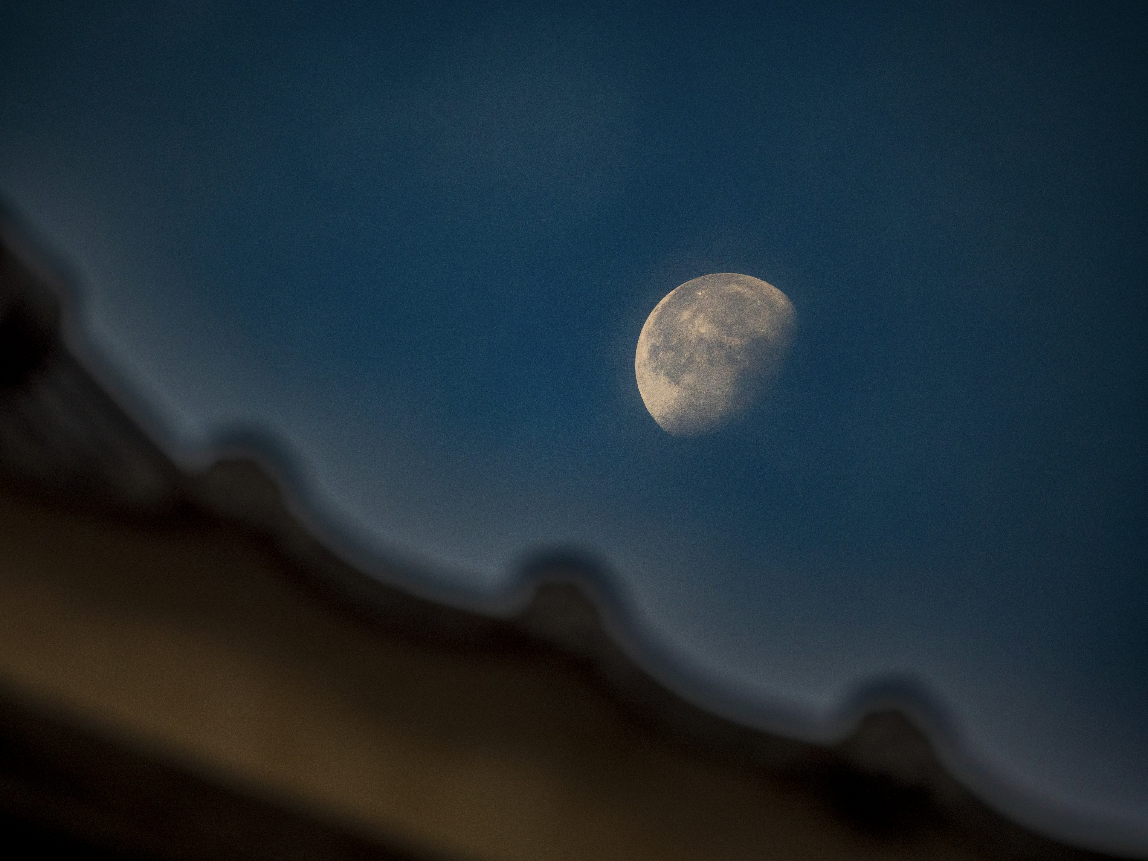 Half moon in a blue sky with a roof silhouette