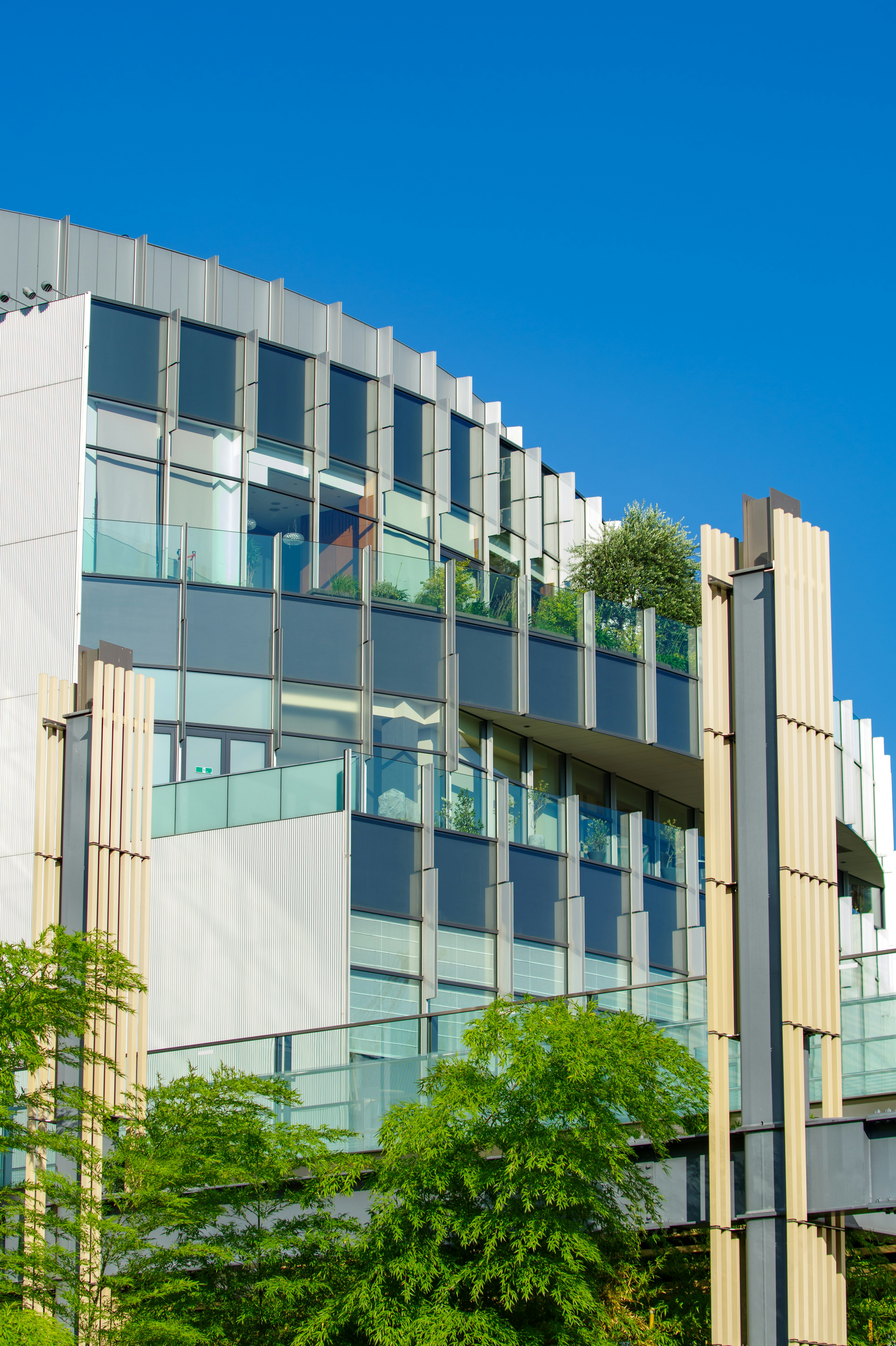 Façade moderne d'immeuble avec balcons en verre et verdure