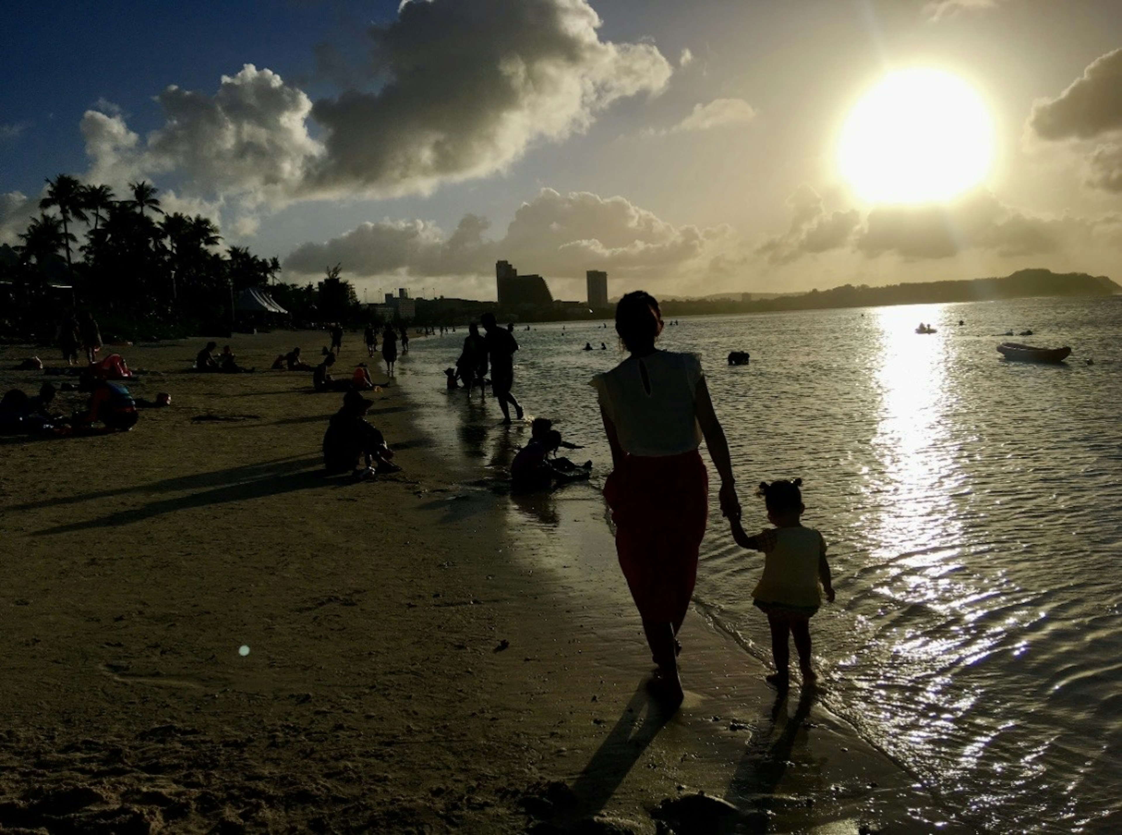 夕日を背にした母親と子供のシルエットが海岸を歩いている