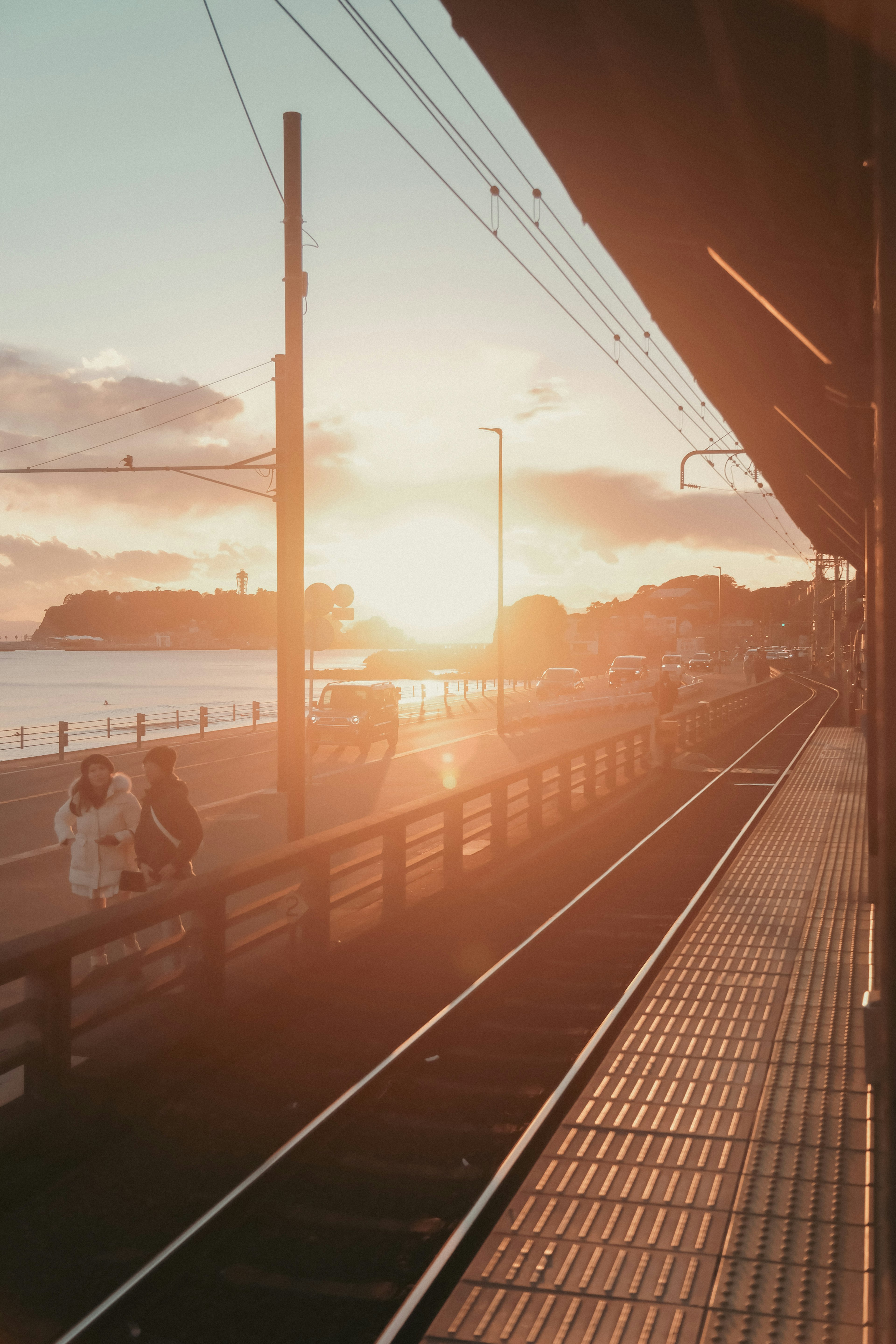 Sunset at a seaside train station with silhouettes of people