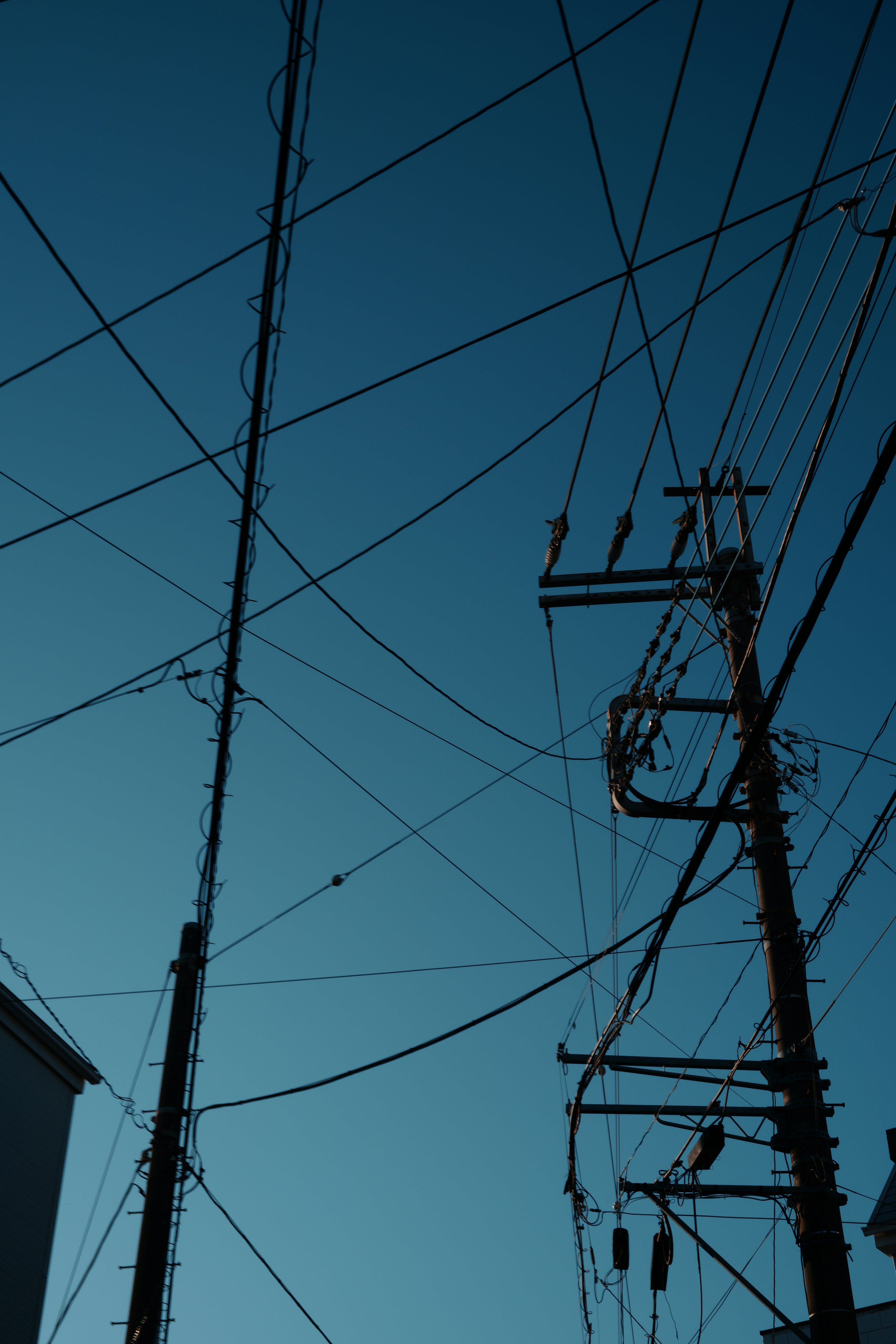 Silhouettes of utility poles and wires against a blue sky