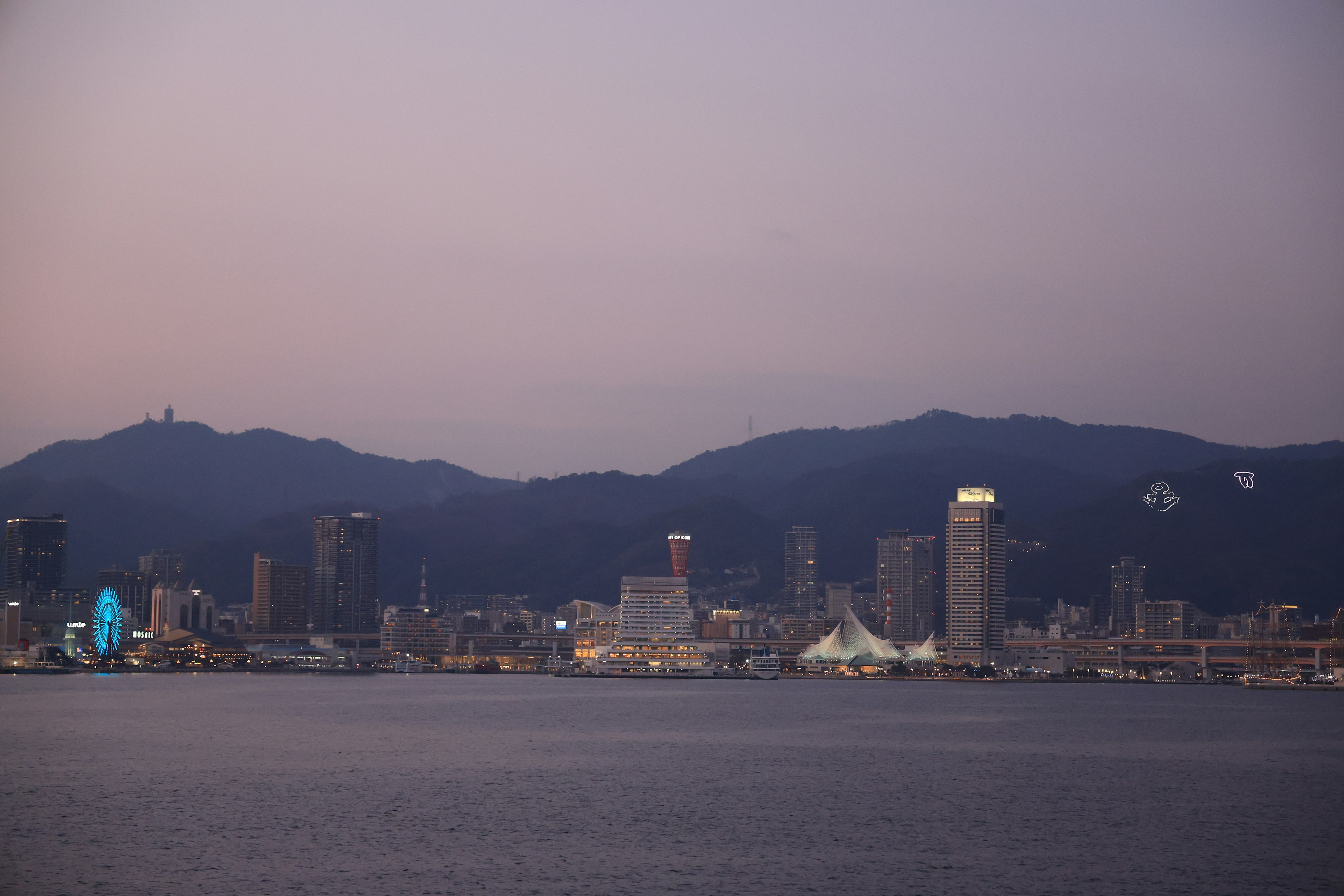 Horizonte de la ciudad al atardecer con montañas al fondo y reflejos en el agua