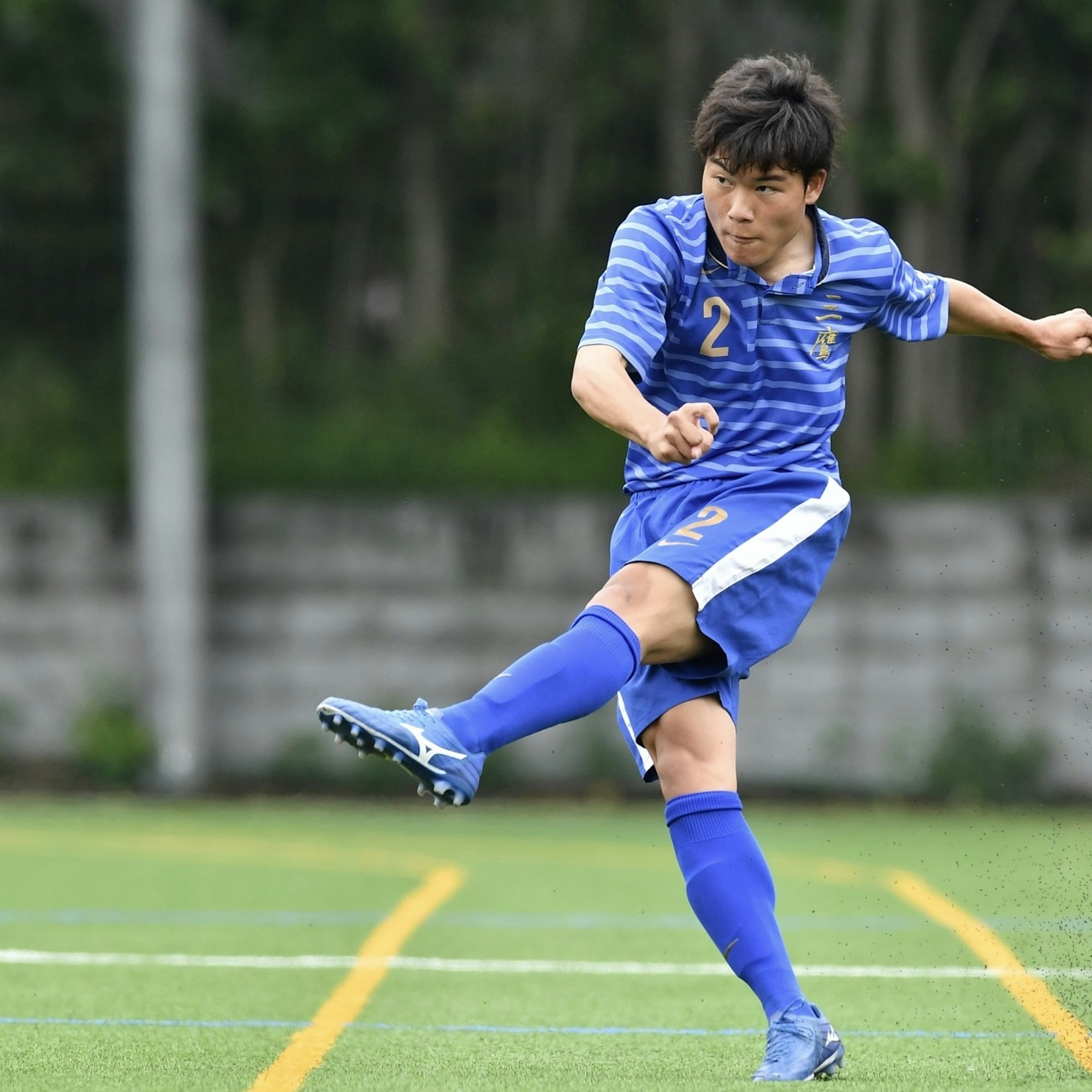 Giocatore di calcio che calcia un pallone indossando un'uniforme blu e pantaloni corti con il numero 2 visibile