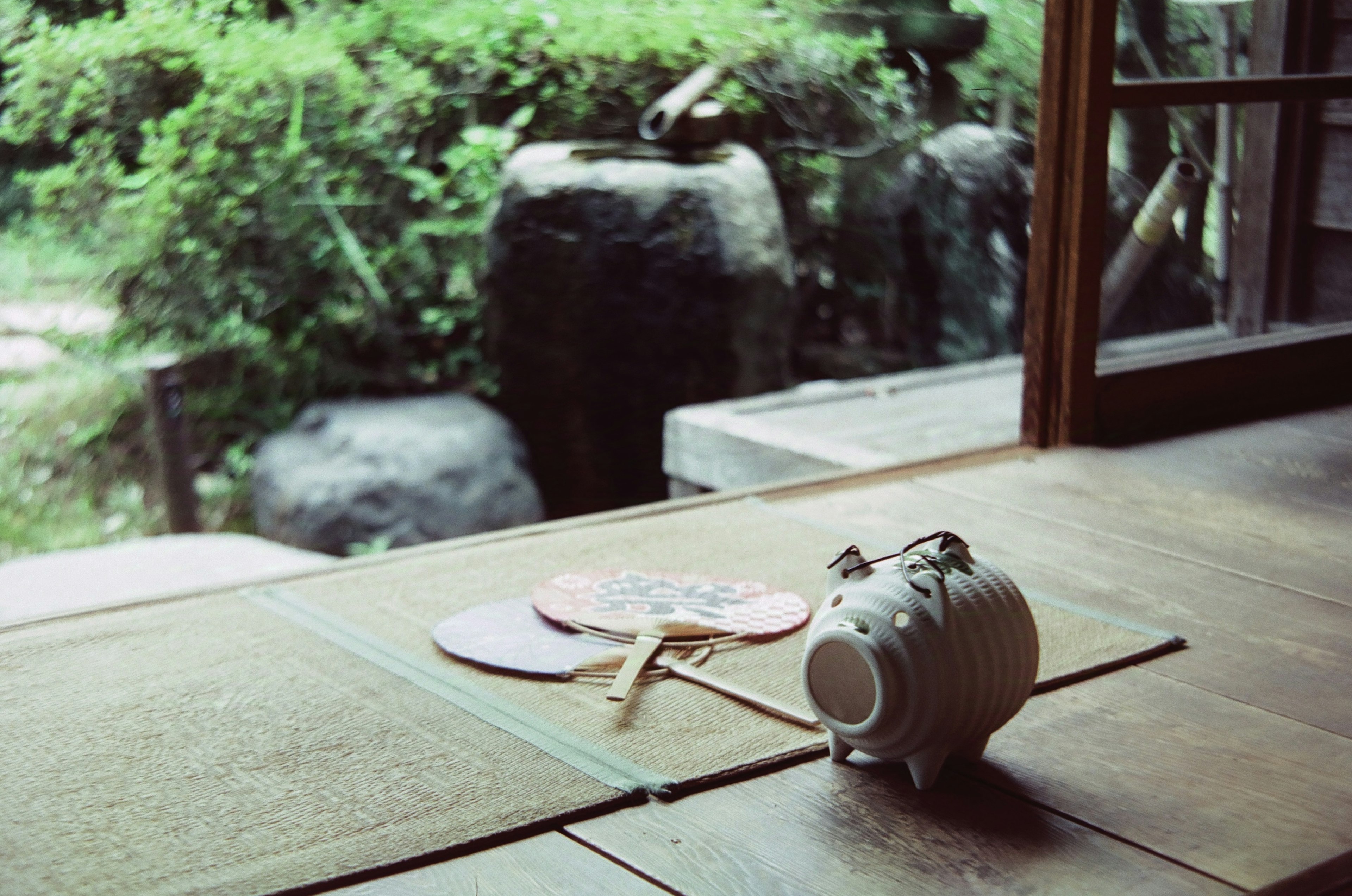 Una alcancía en forma de cerdo y un abanico sobre una mesa de madera en una habitación de estilo japonés con vista a un jardín verde