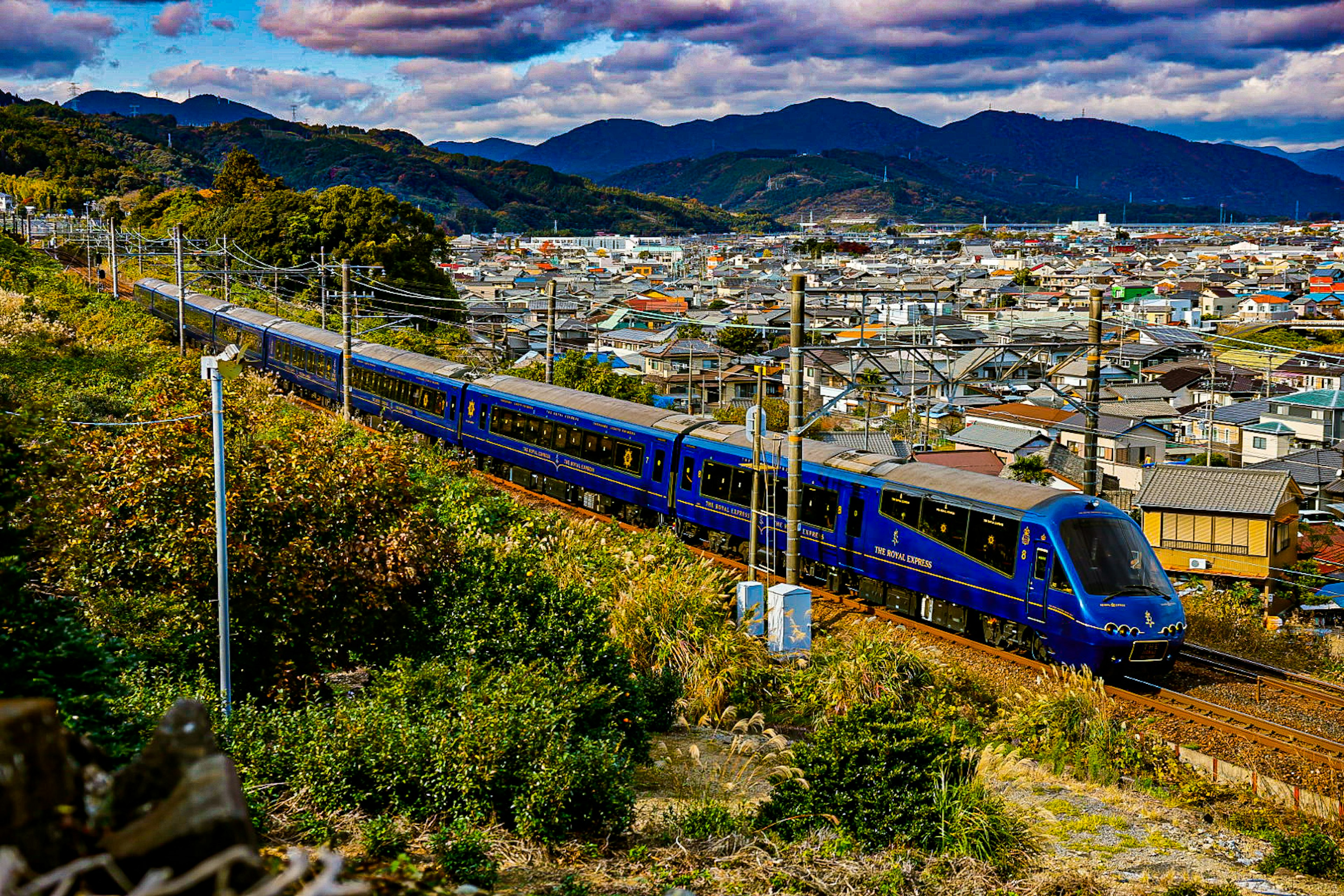 青い列車が山の背景を背にして走っている街の風景