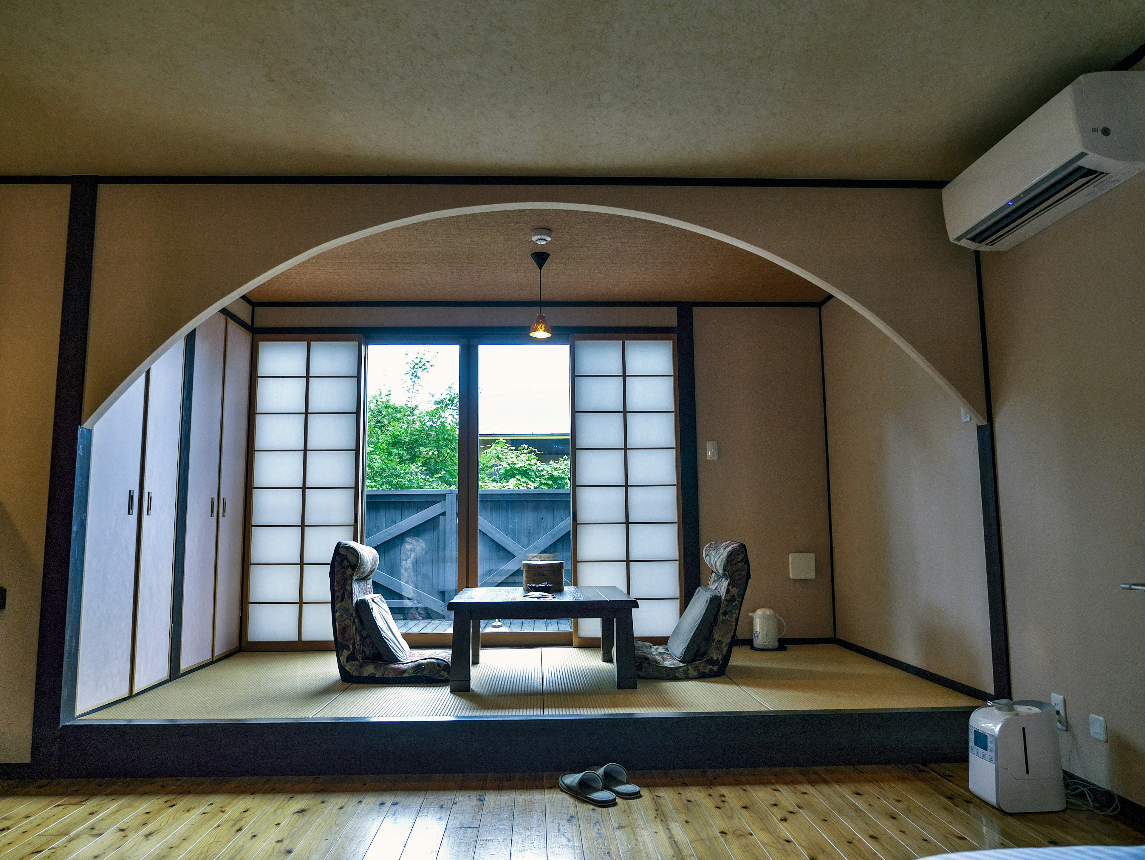 Japanisch eingerichtetes Wohnzimmer mit Tisch und Stühlen, die durch große Fenster auf einen Garten blicken