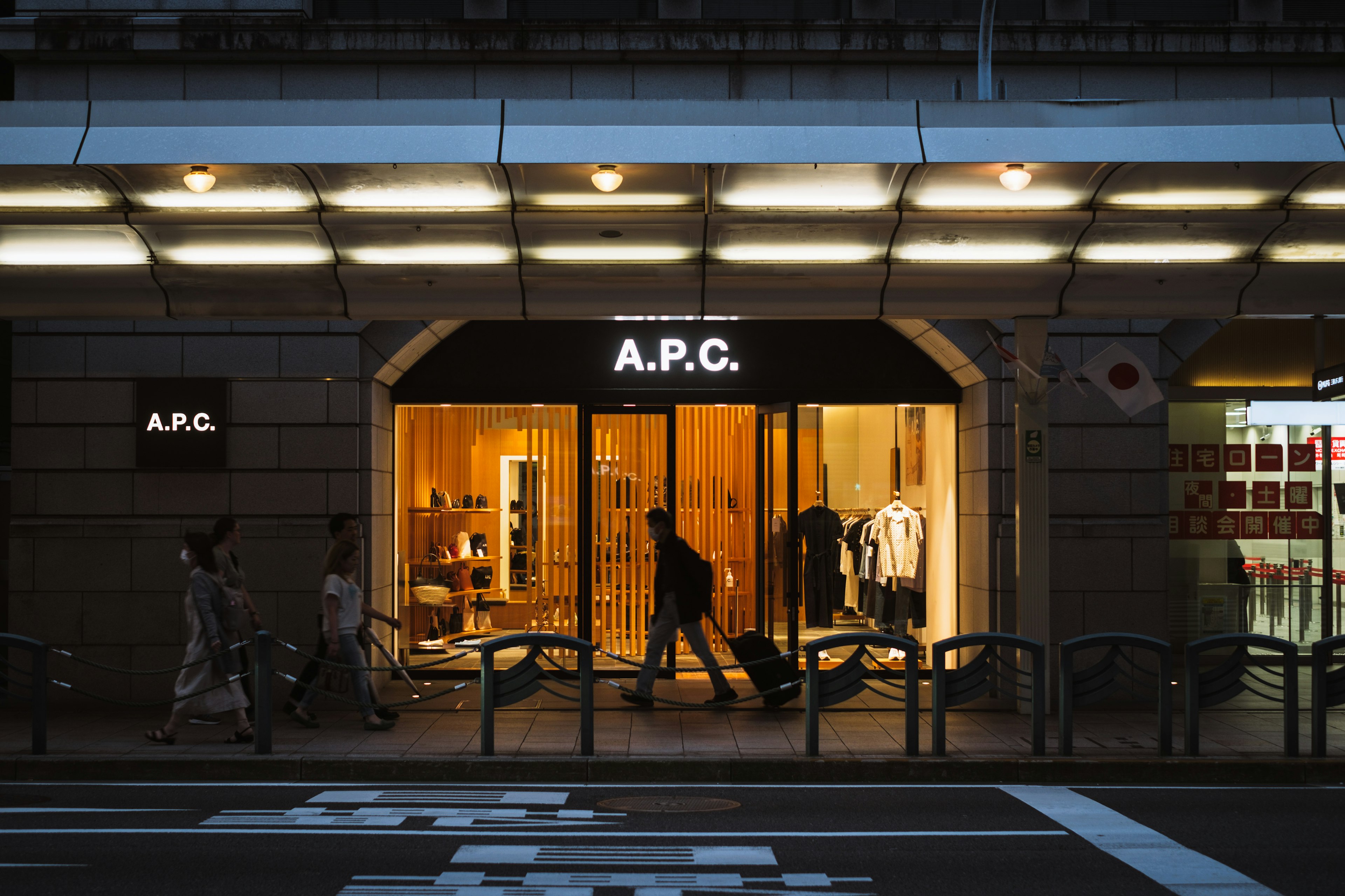 A.P.C. store illuminated at night with pedestrians walking by