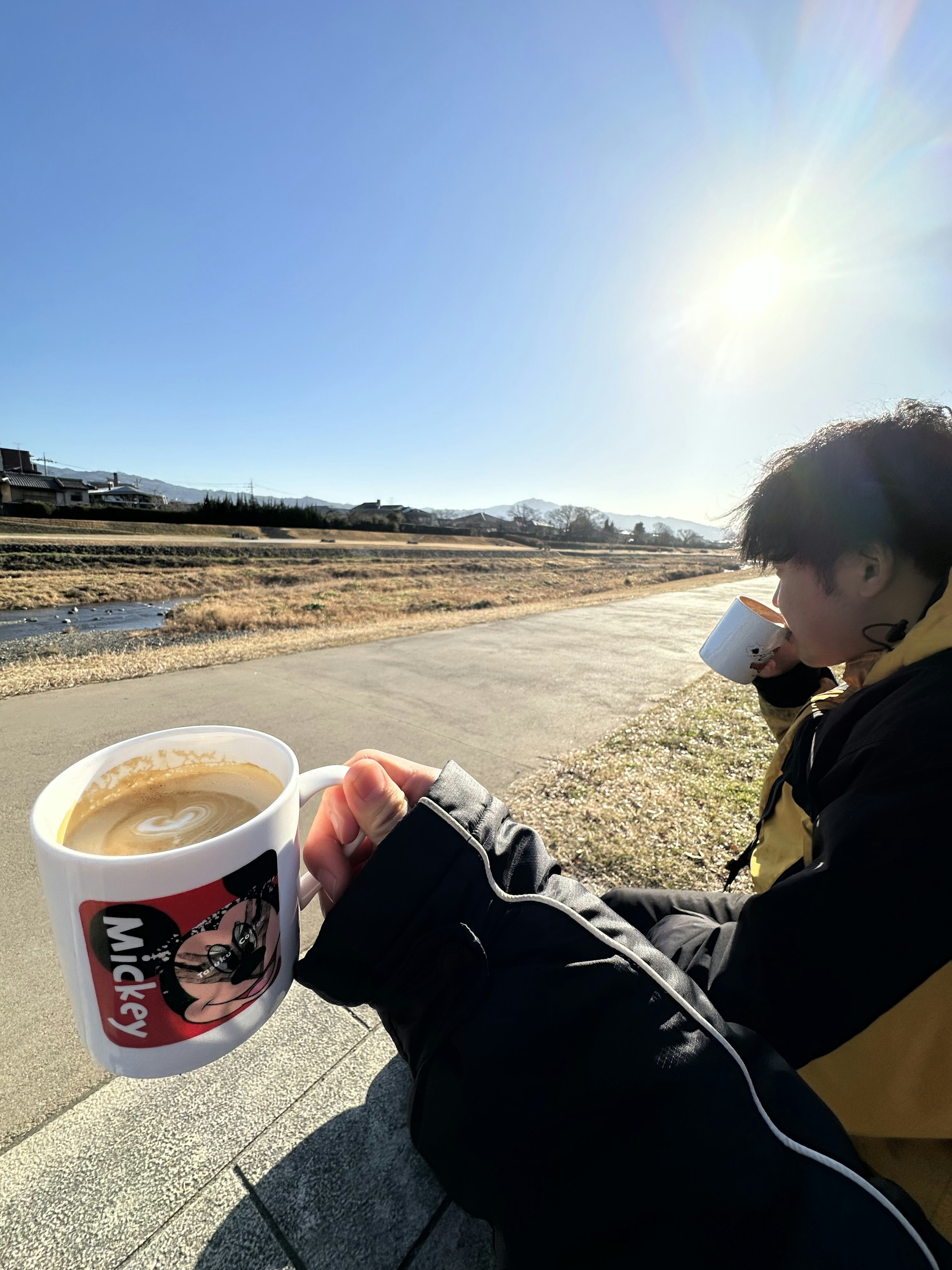 Un giovane che beve caffè in una giornata di sole con un paesaggio naturale sullo sfondo