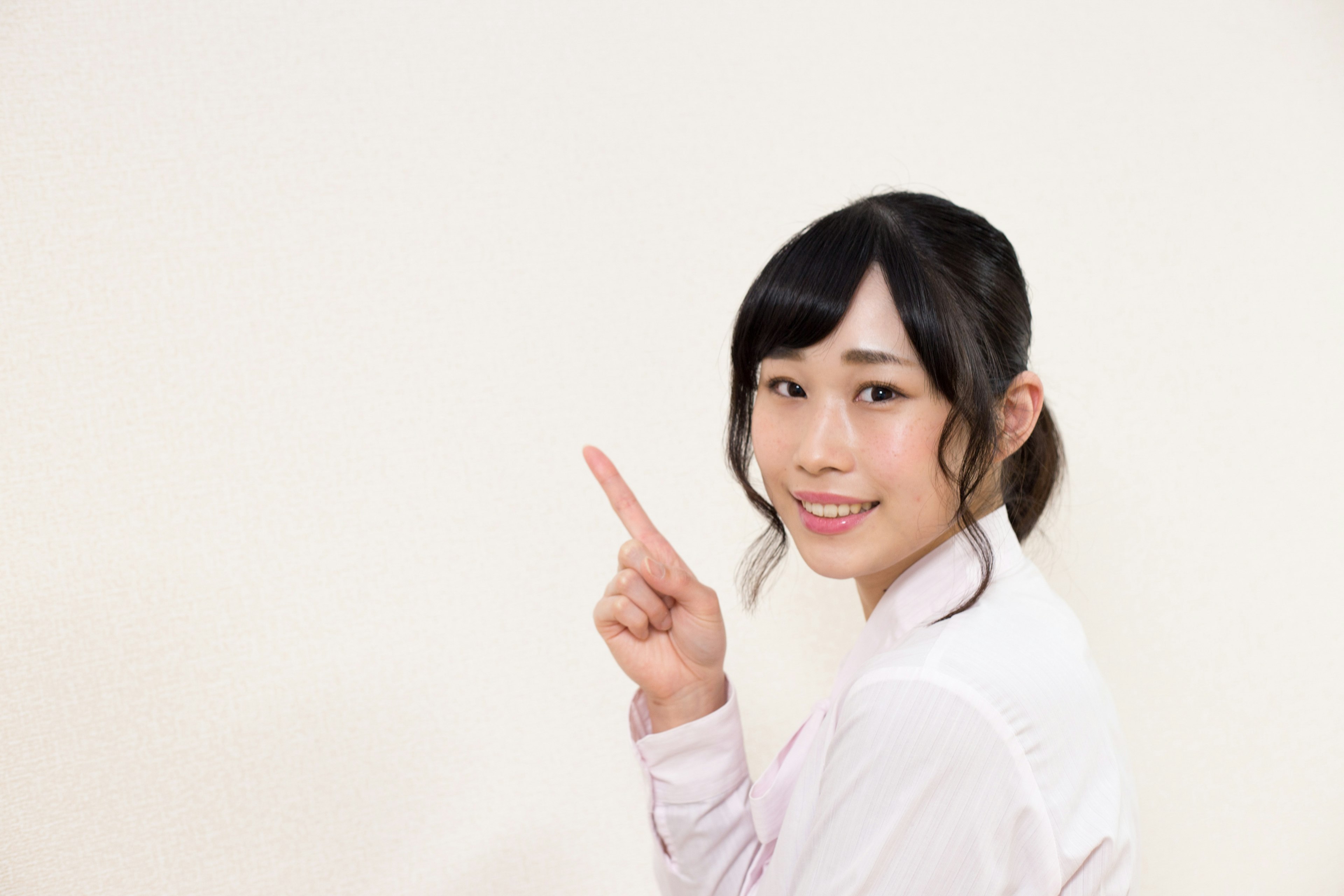 Smiling woman pointing with one finger in front of a white background