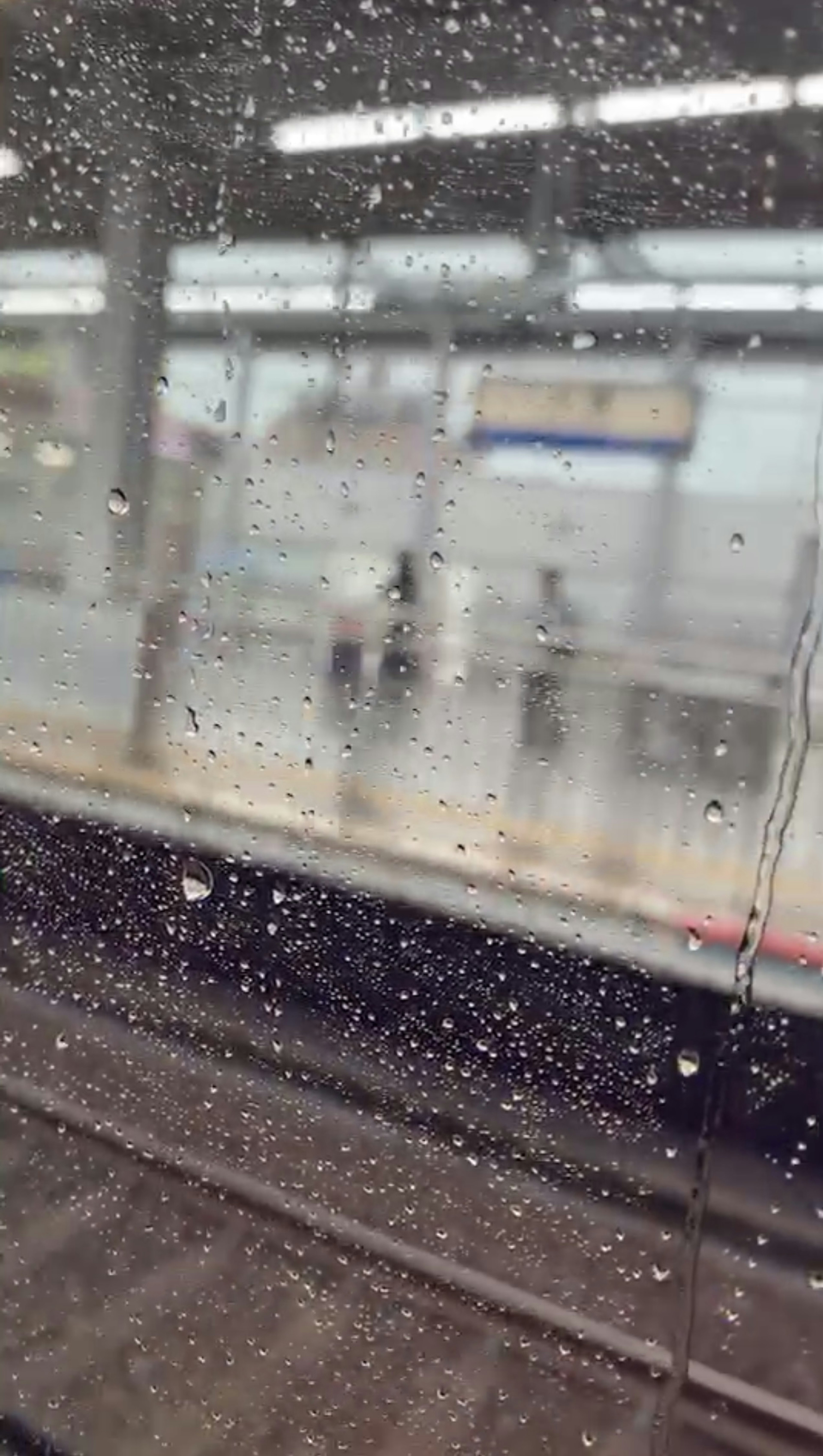 Blick auf einen Bahnhof durch ein regennasses Fenster mit verschwommenen Figuren