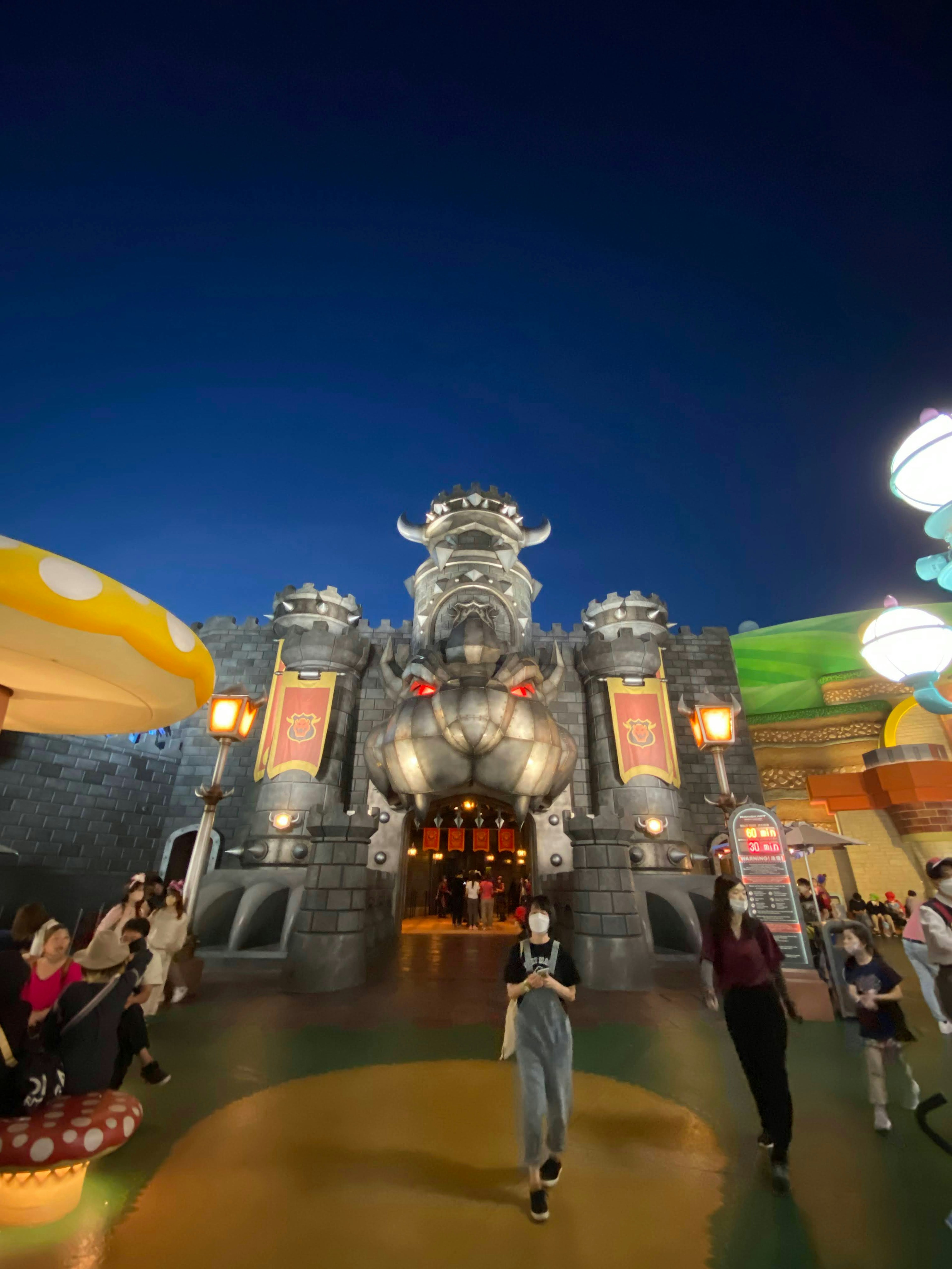 Entrada de un parque de atracciones con una gran escultura y diseños coloridos por la noche