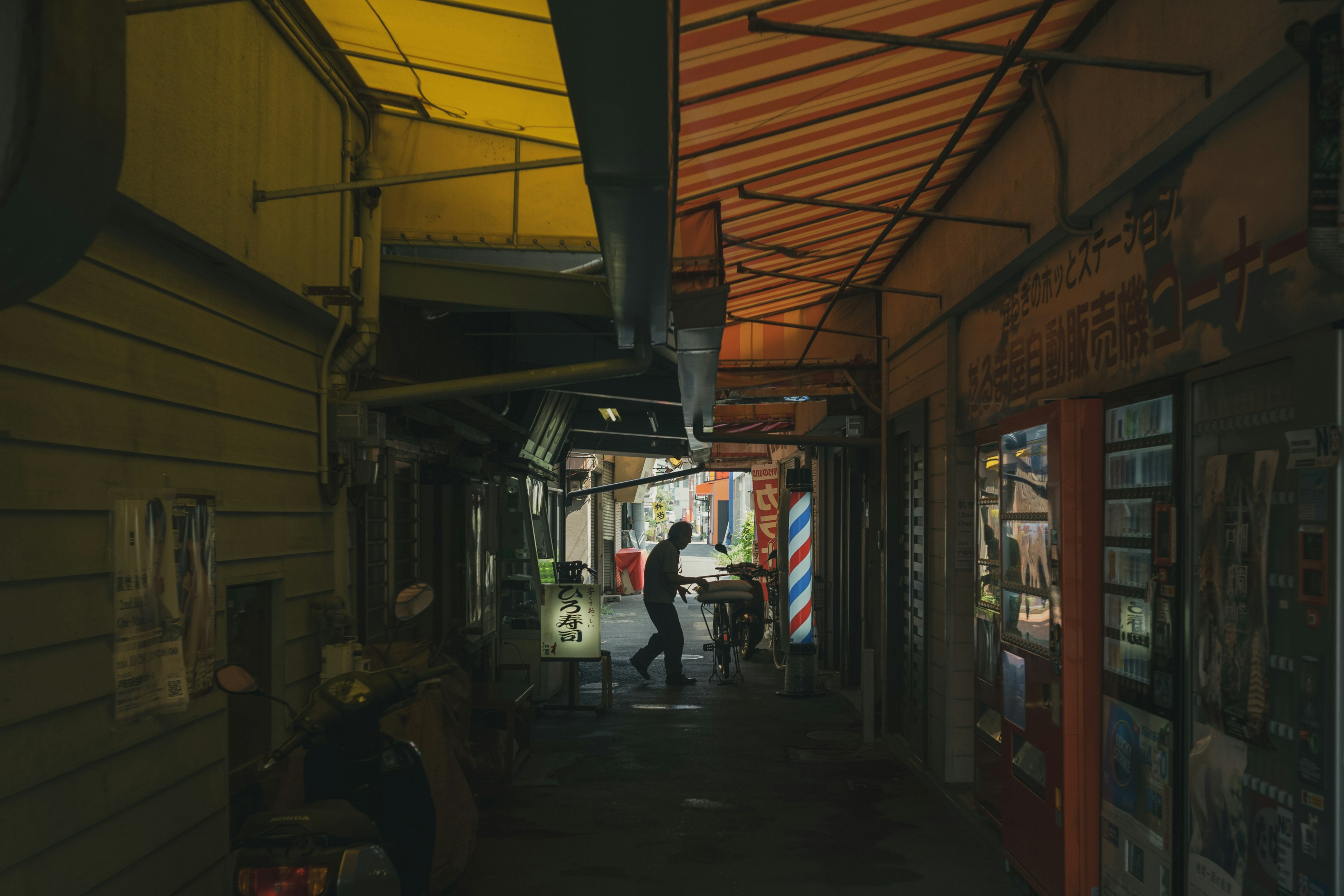 A narrow alley with a person walking Various colored awnings and clutter in front of shops