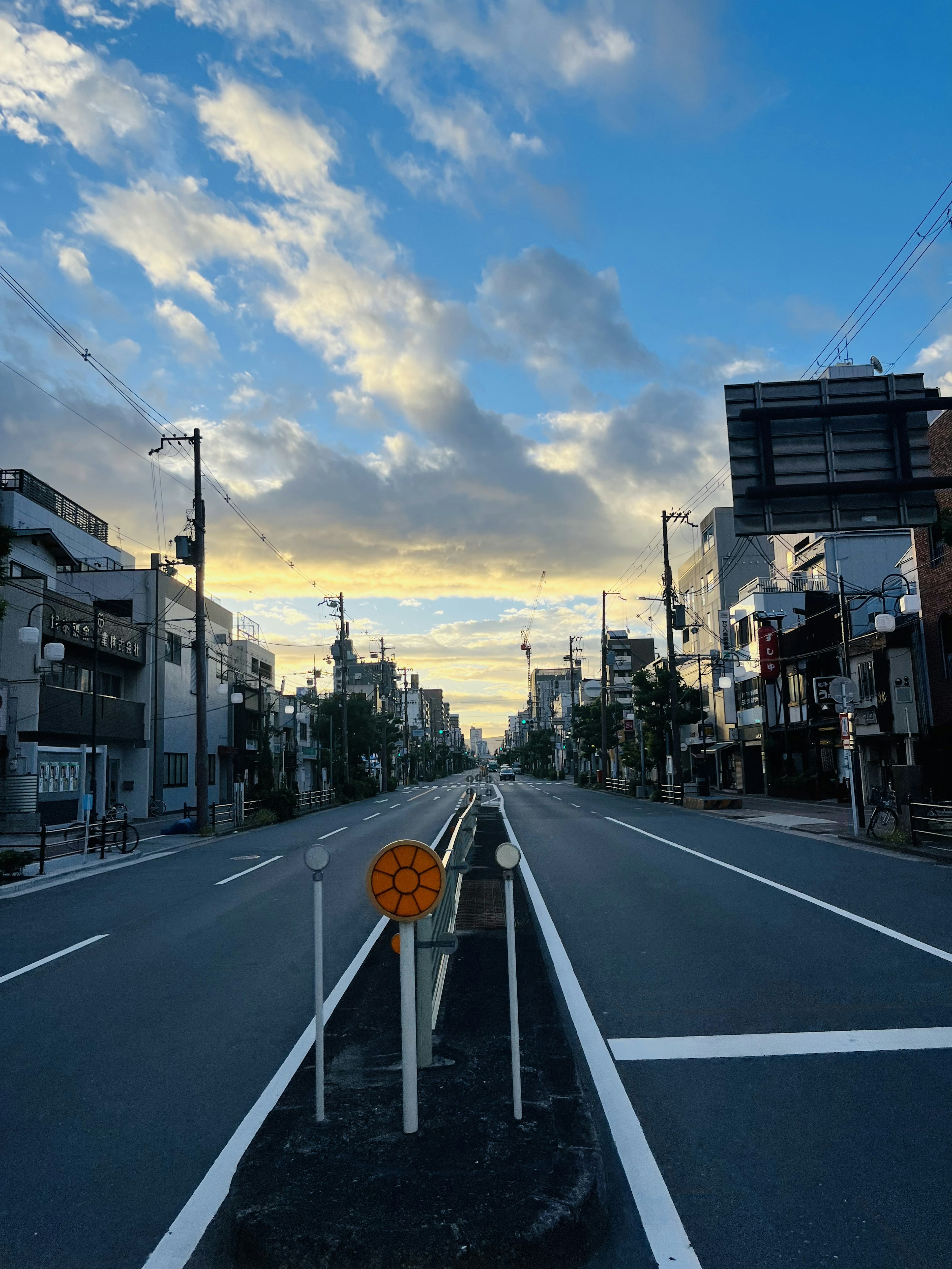 青空と雲が広がる街の通りにオレンジ色の標識が立つ