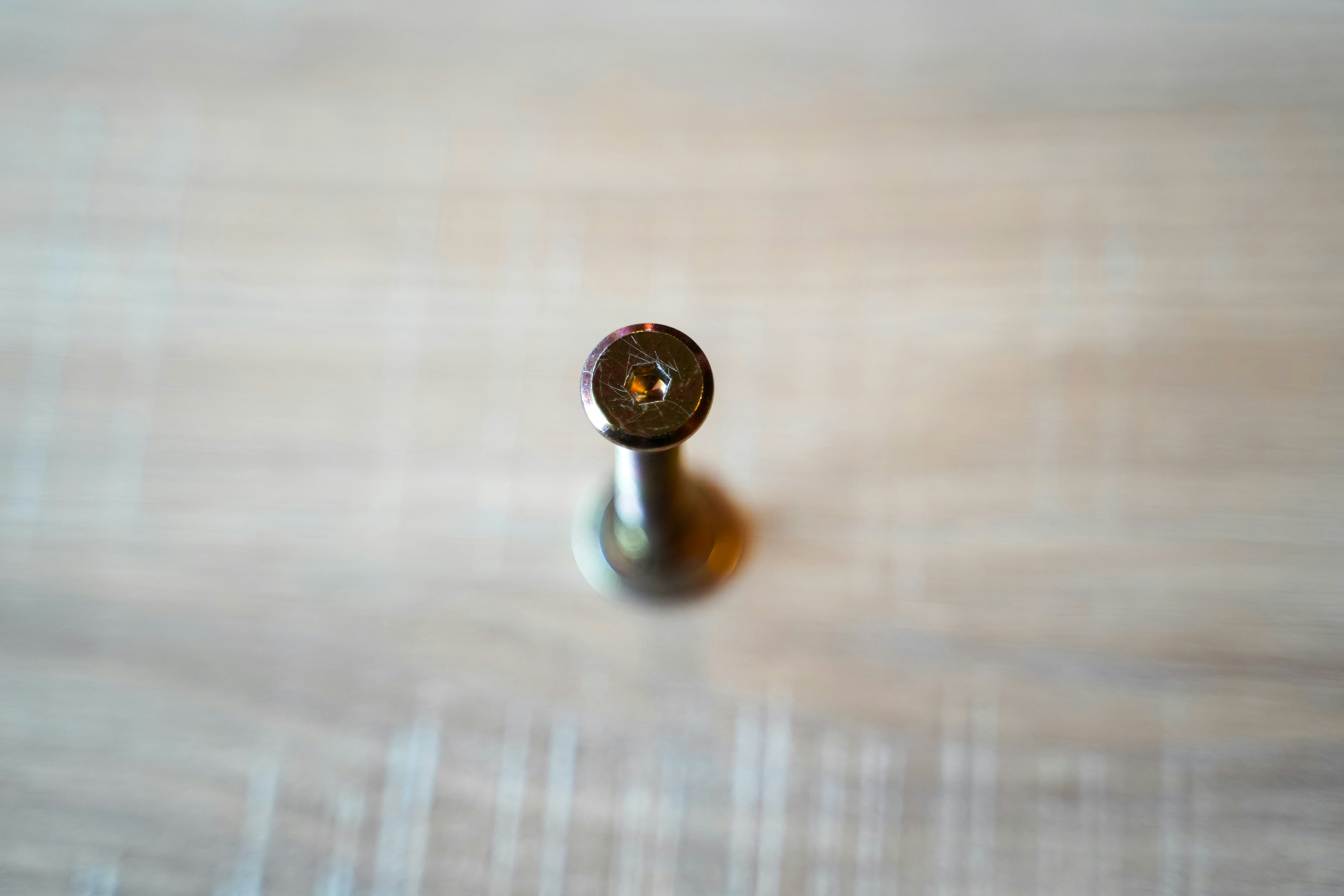 Close-up of a metal nail viewed from above resting on a wooden surface