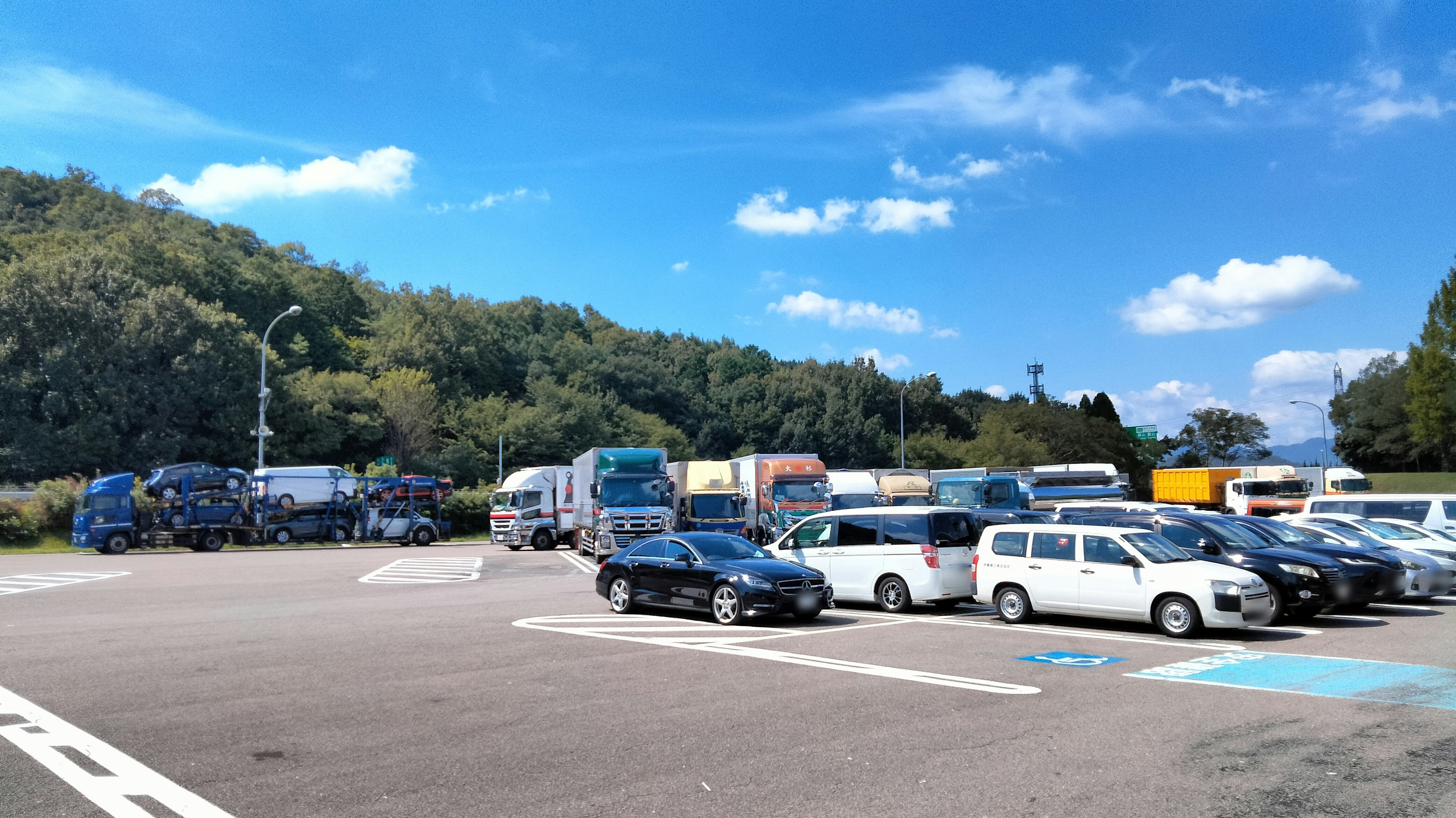 A scene of trucks and cars parked with a blue sky and green hills in the background