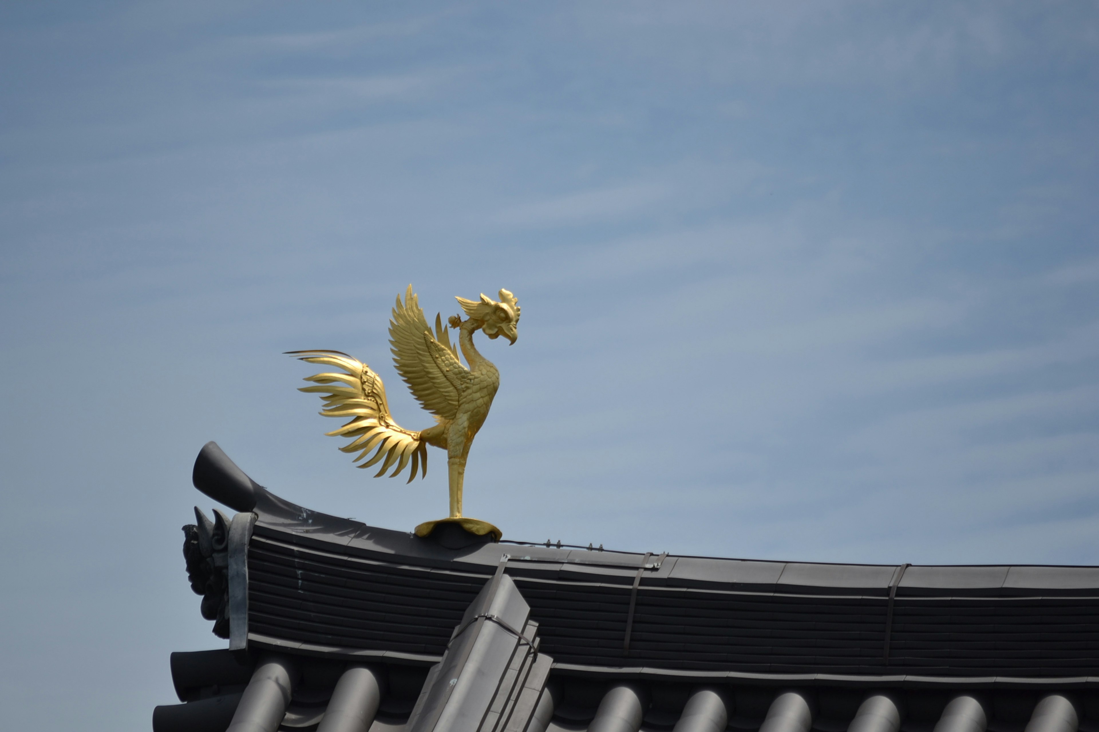 Scultura di gallo dorato su un tetto contro un cielo blu