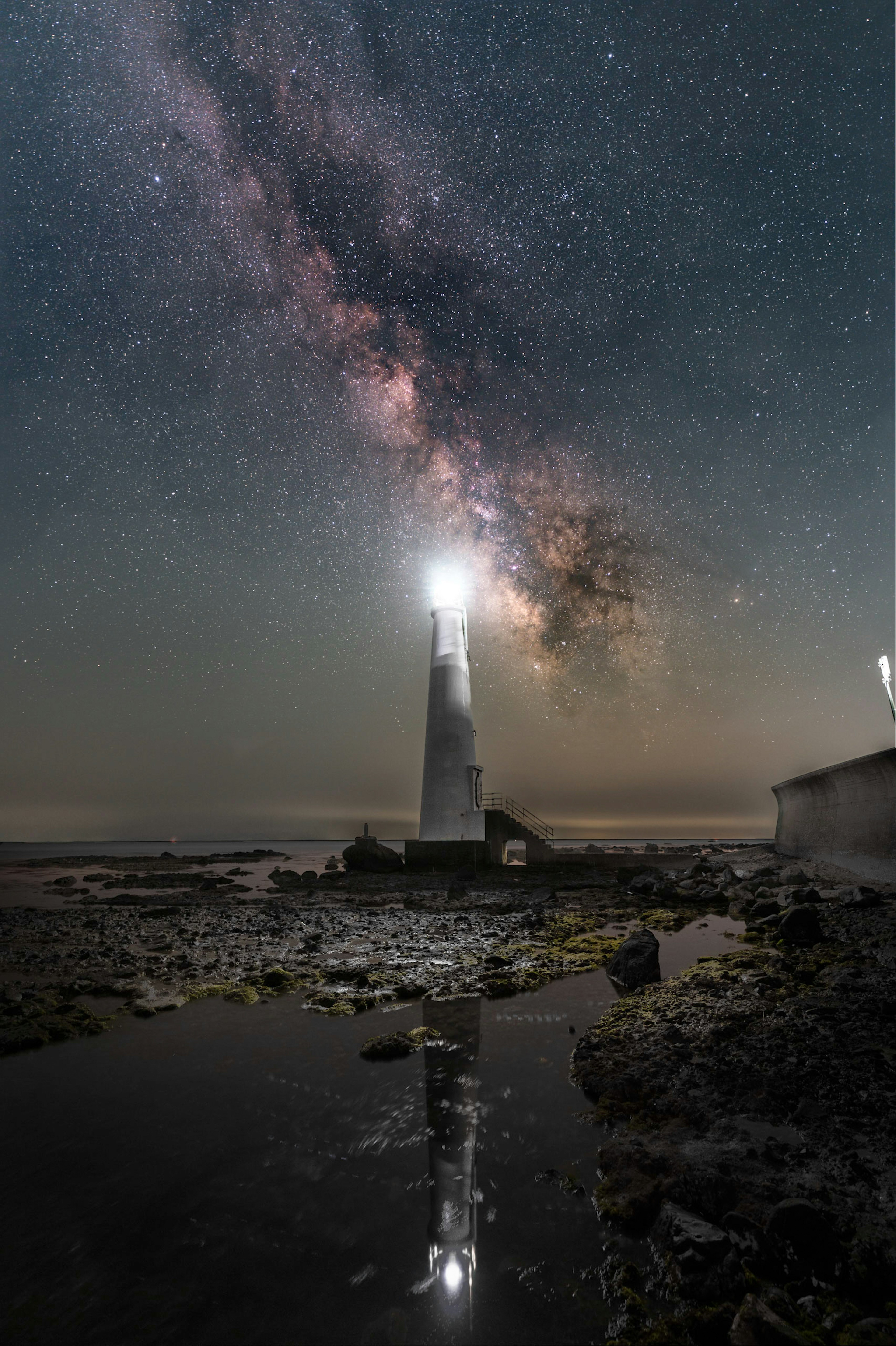 星空の下に立つ灯台とその反射が水面に映る美しい風景