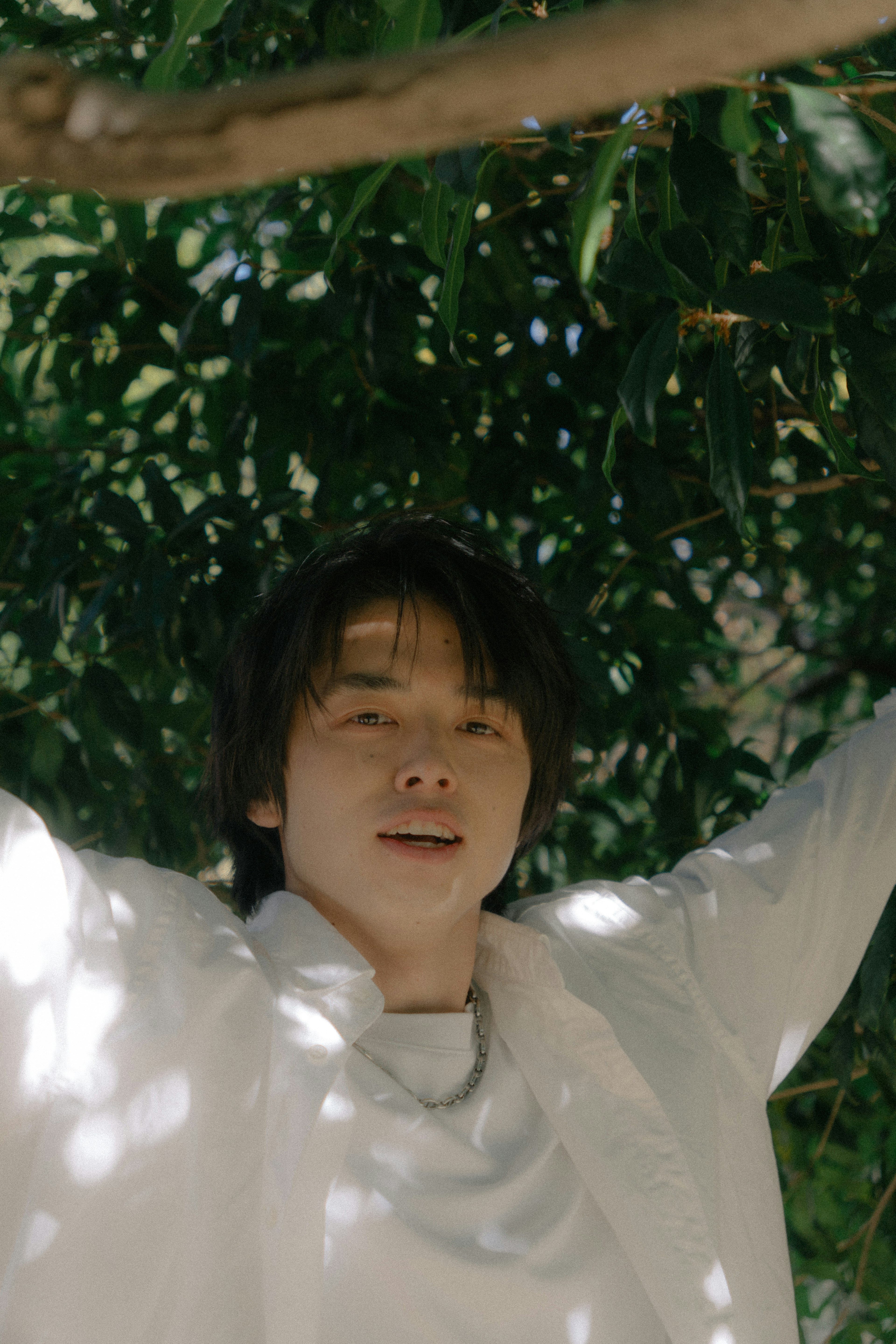 Young man smiling under a tree wearing a white outfit