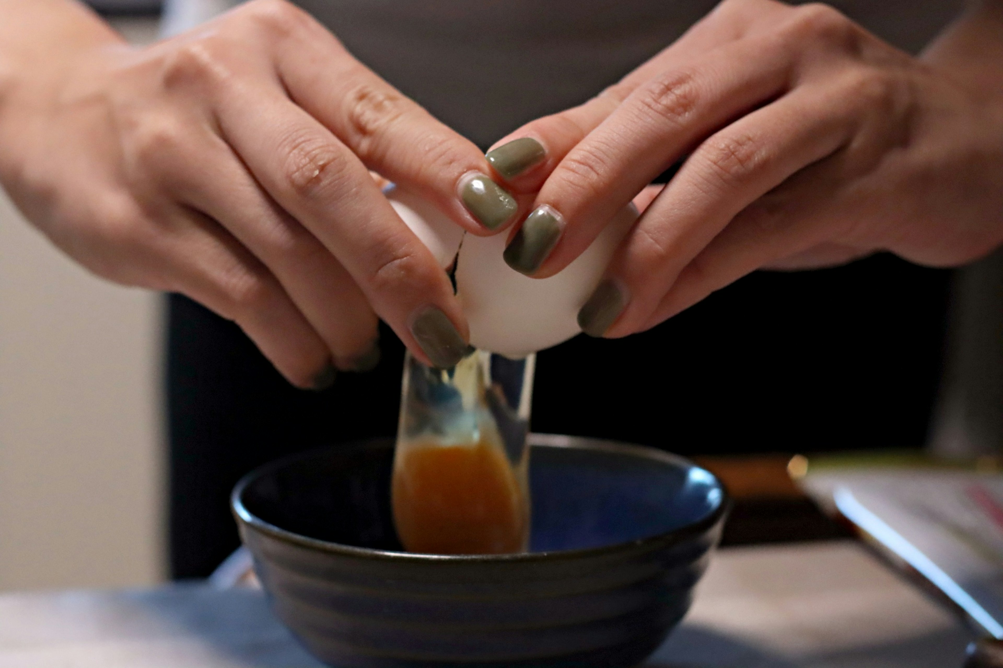 Hands cracking an egg into a bowl with yolk and egg white