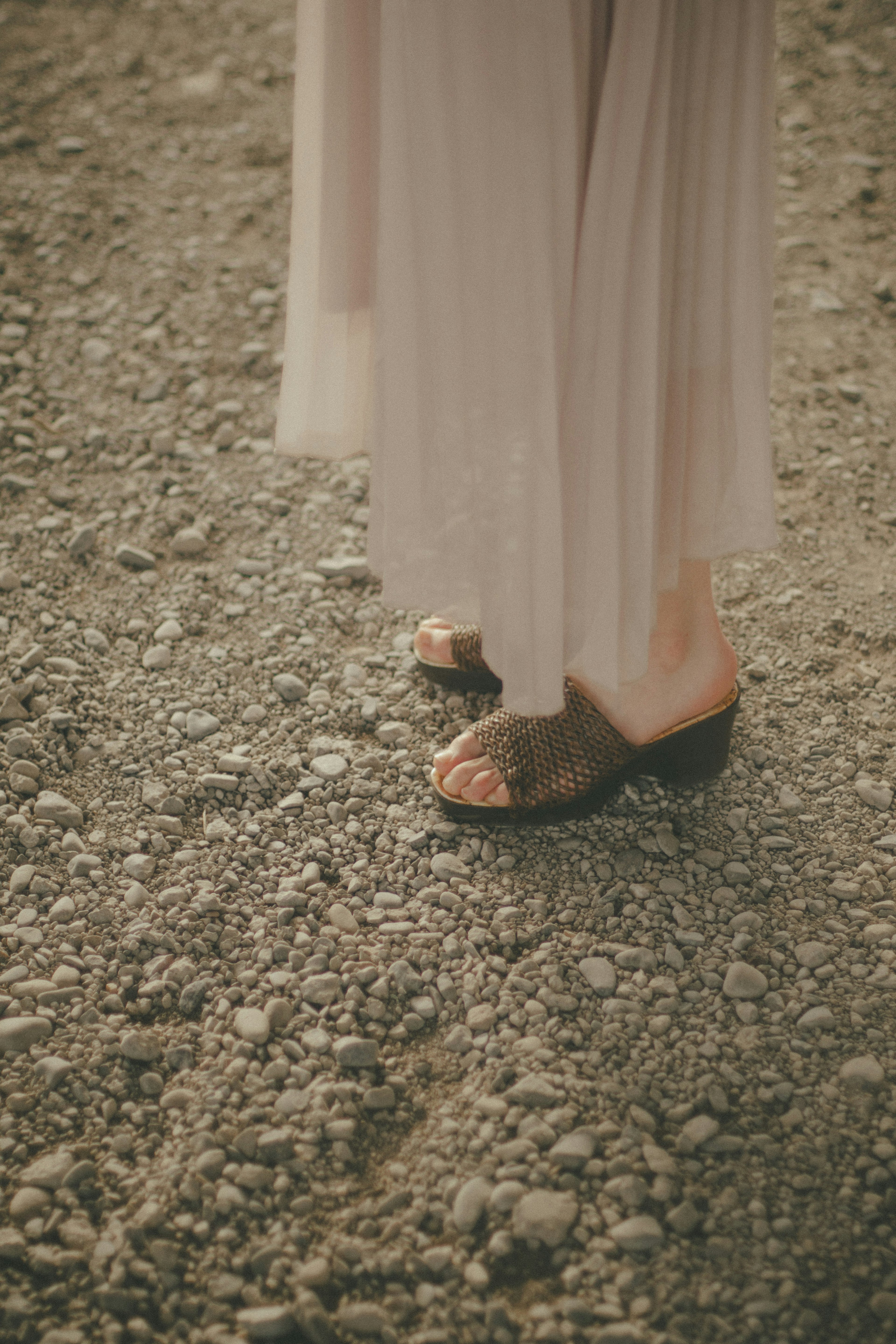 A woman's feet wearing shoes standing on a gravel path