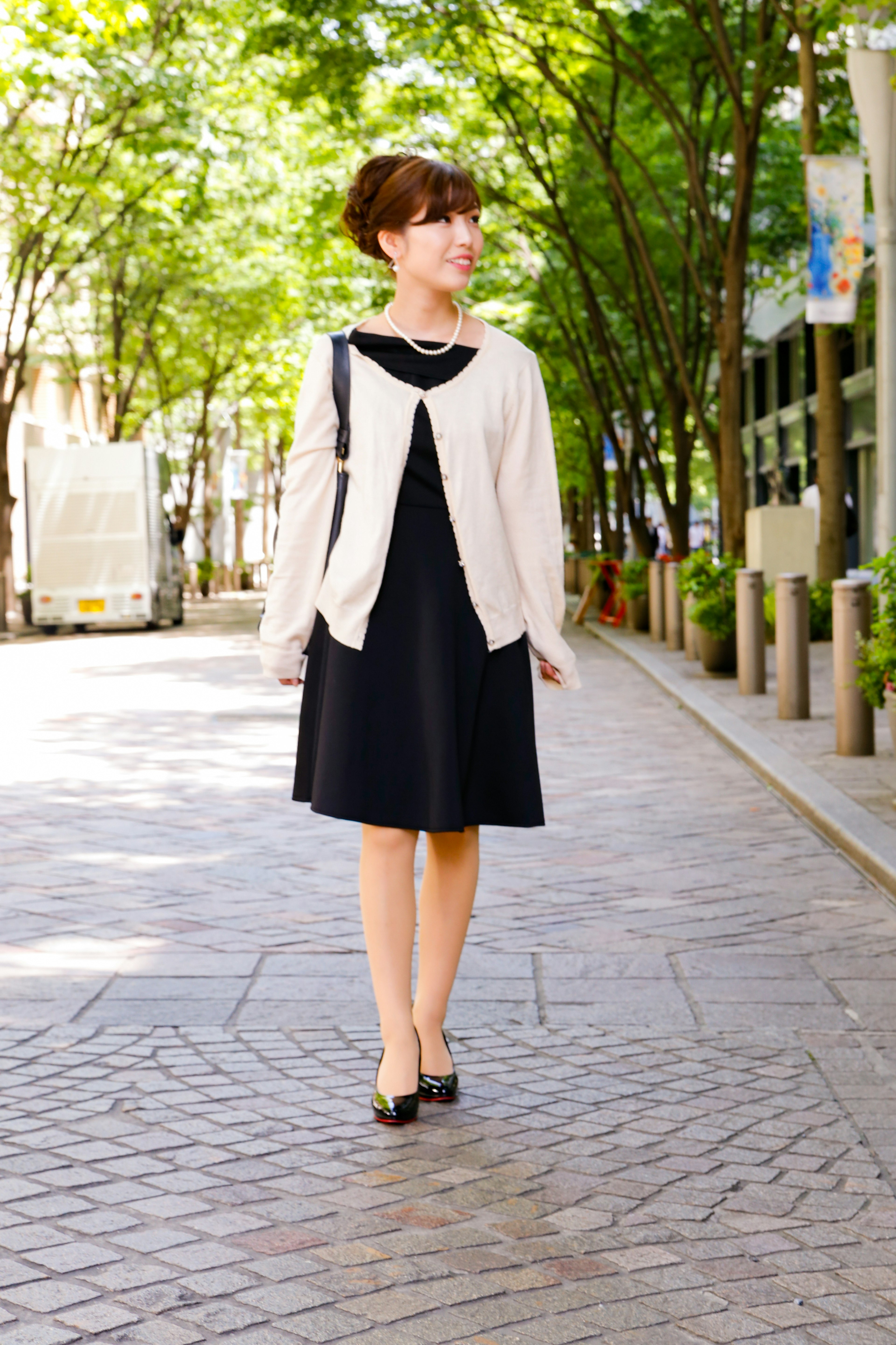 Woman in a black dress and white cardigan walking in a city street