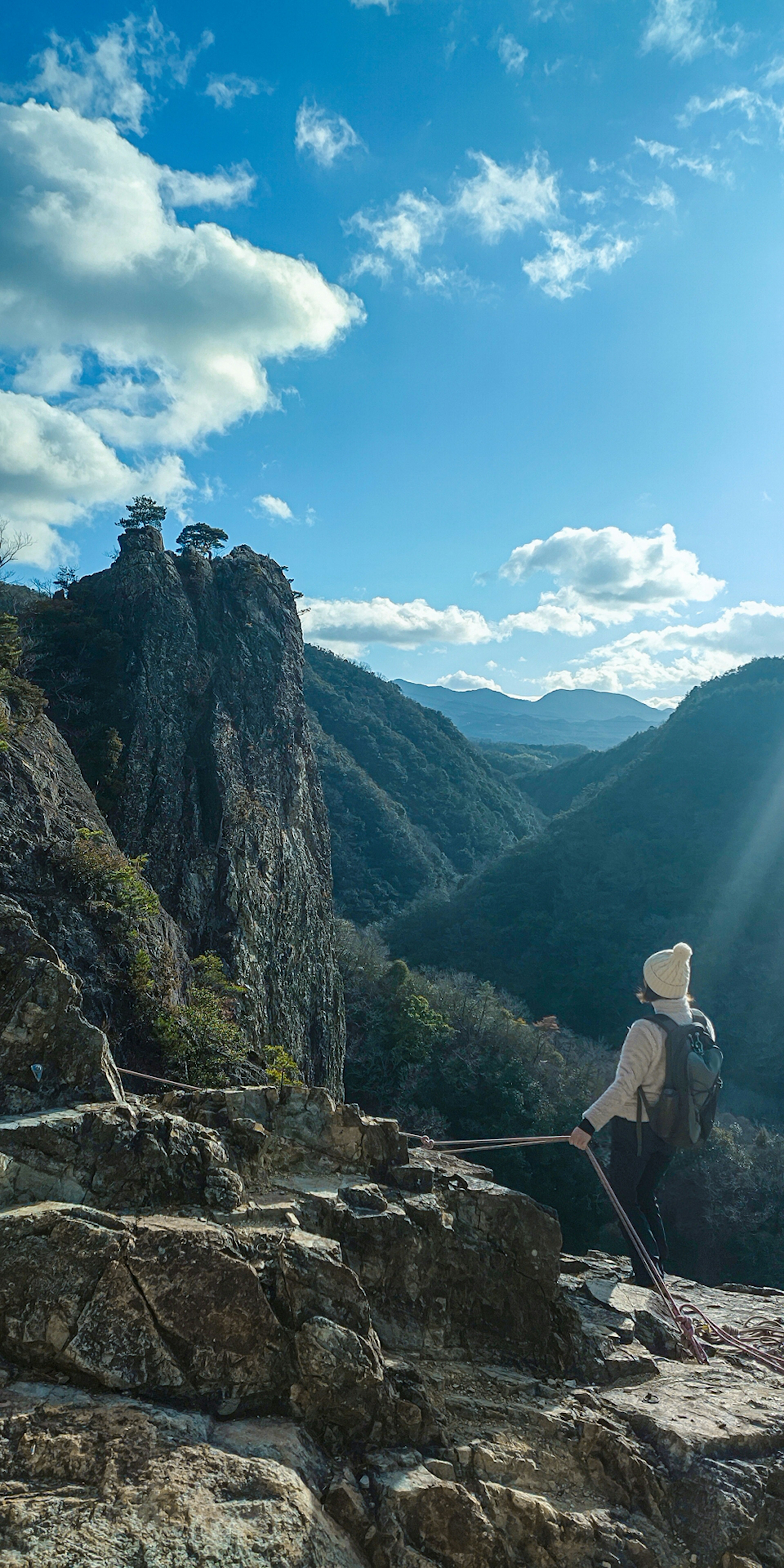 Senderista contemplando un paisaje montañoso bajo un cielo azul y nubes