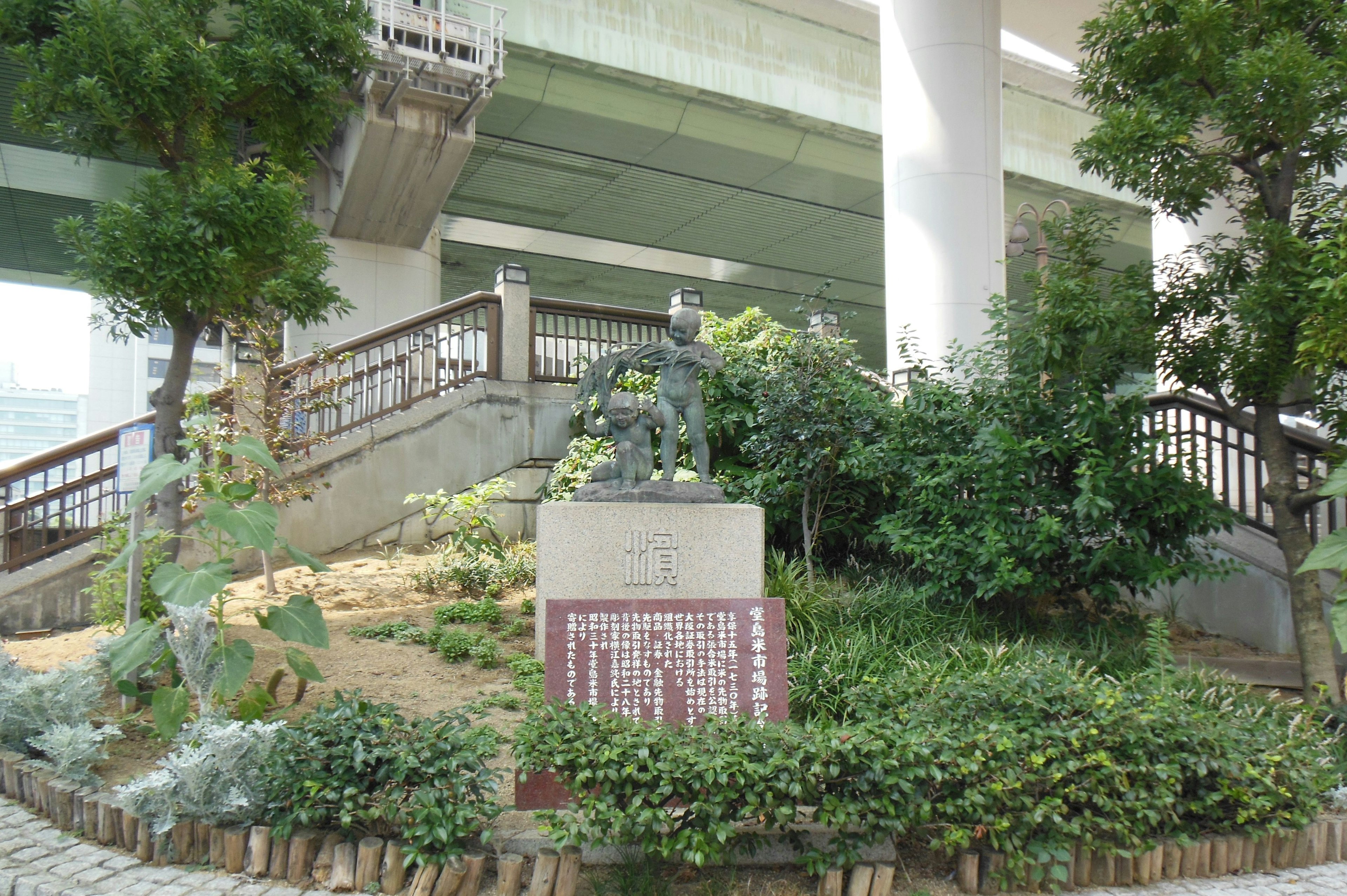 Sculpture and sign in a lush garden under a bridge