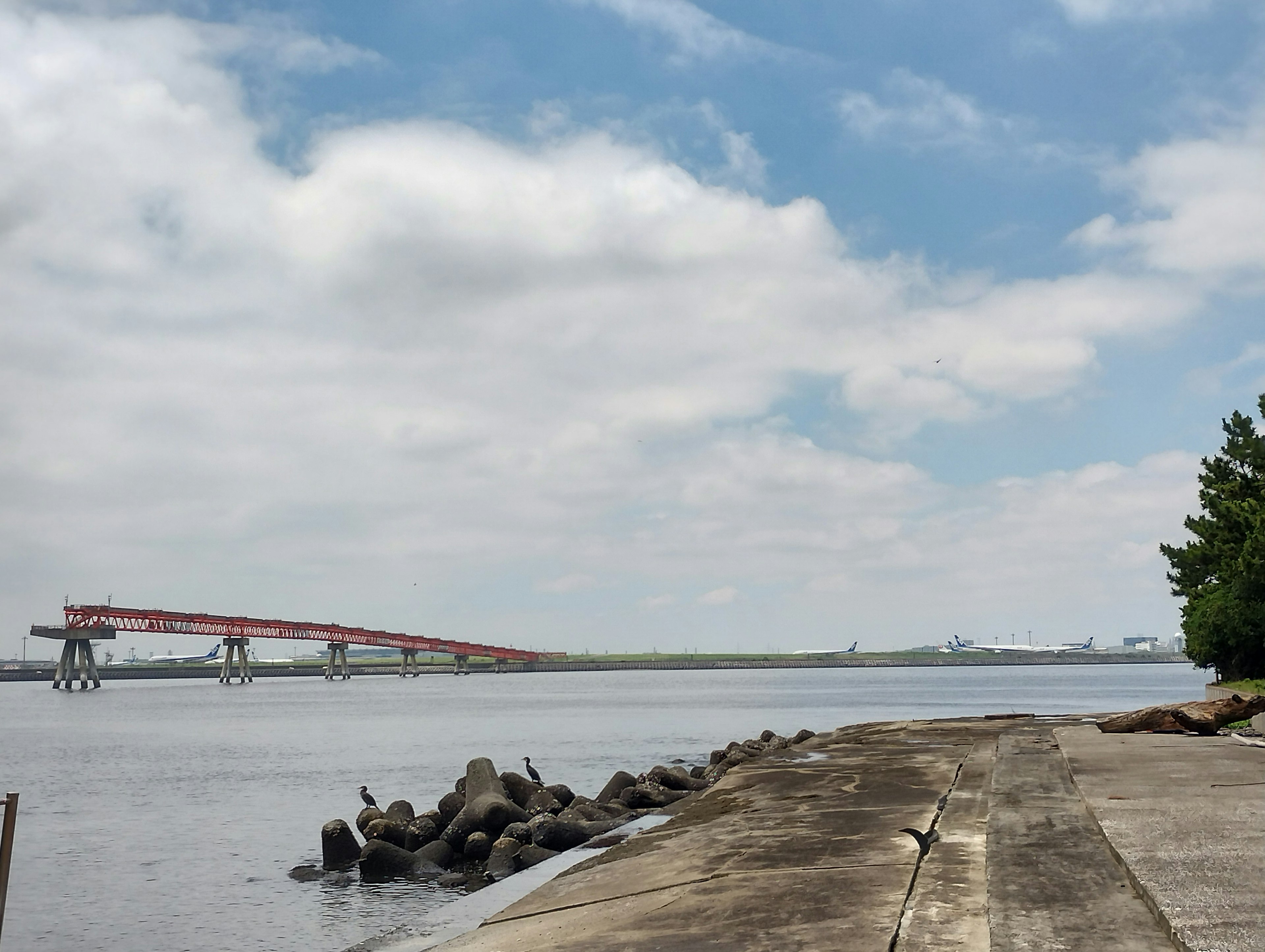 Vista escénica de un camino de concreto a lo largo del río con un puente rojo al fondo