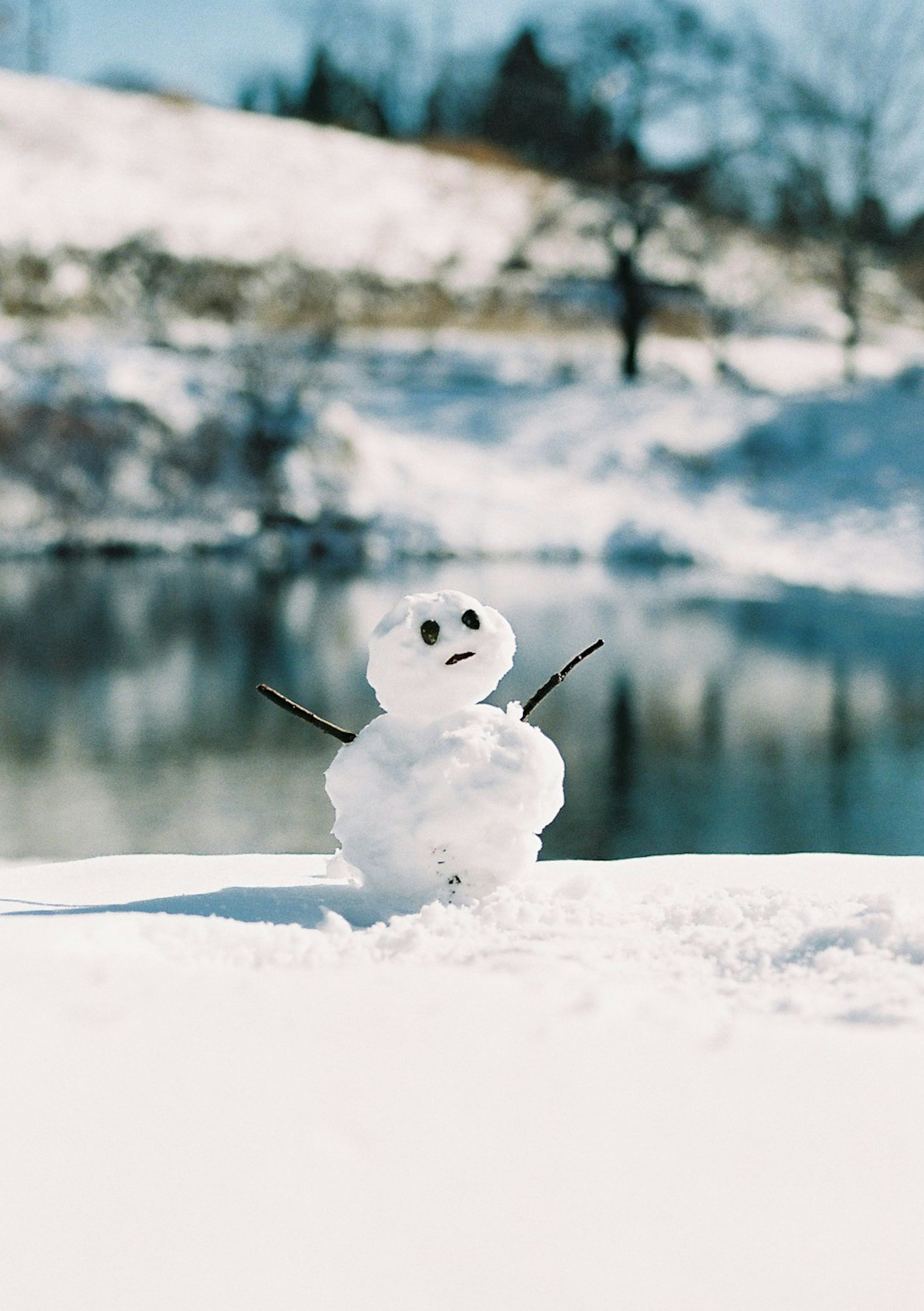 Un petit bonhomme de neige debout dans la neige à côté d'un lac calme