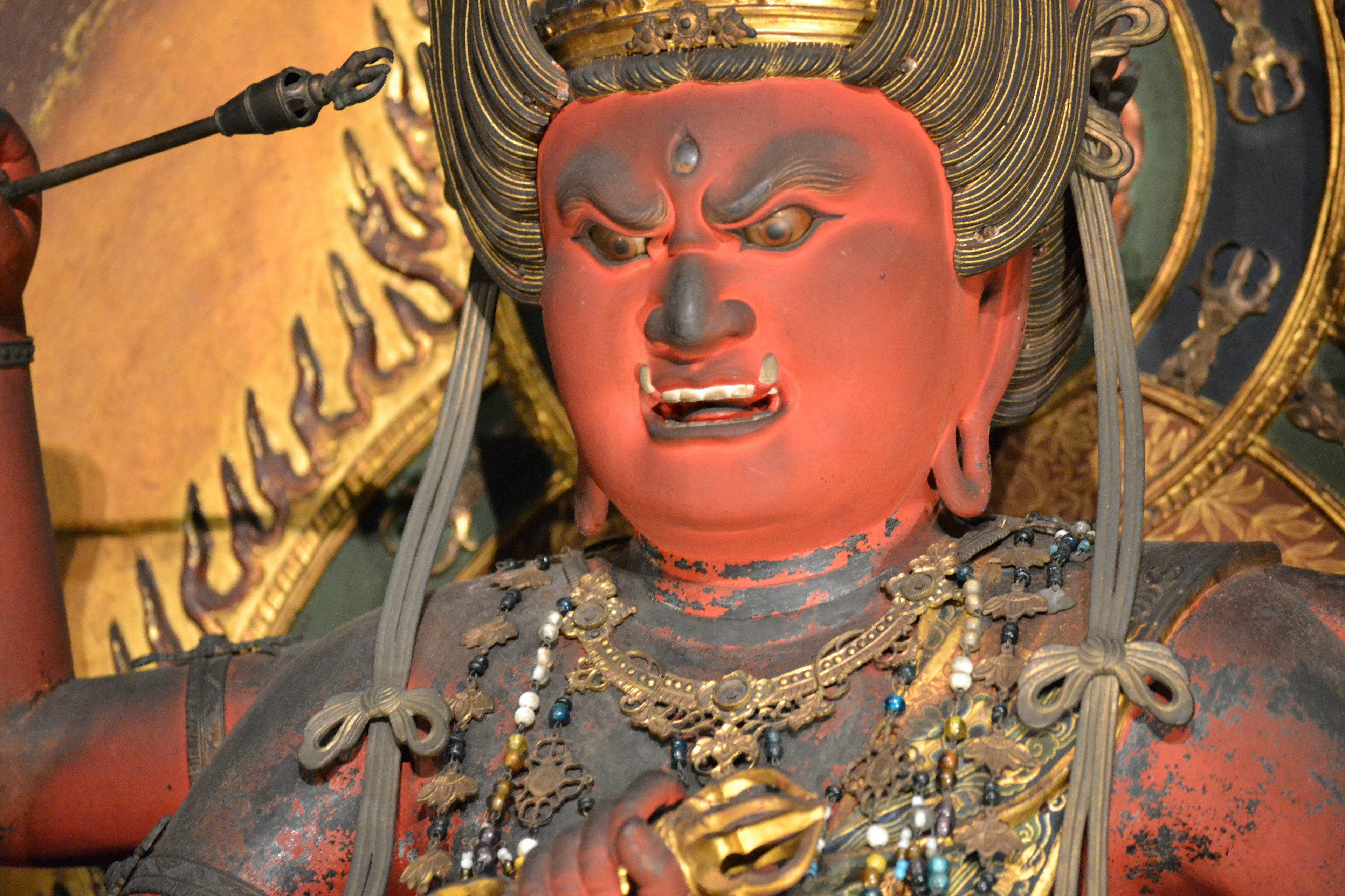 Statue with red skin depicting a fierce deity holding an arrow