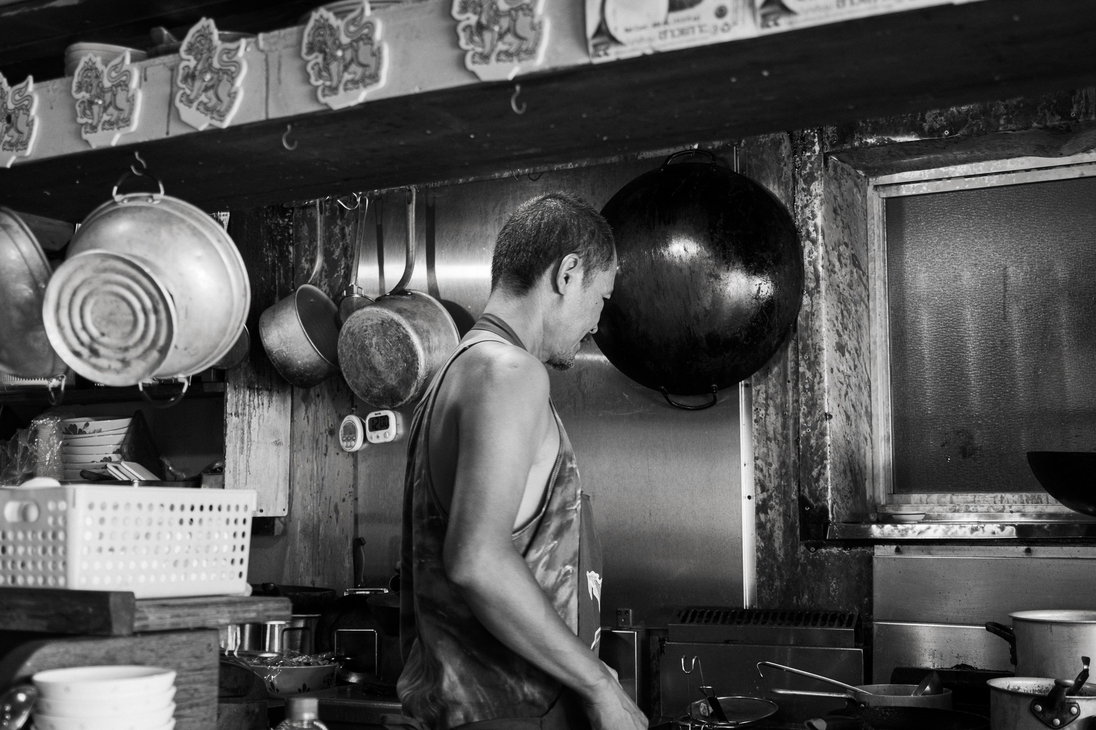 Un homme cuisinant dans une cuisine en noir et blanc entouré de casseroles et de plats