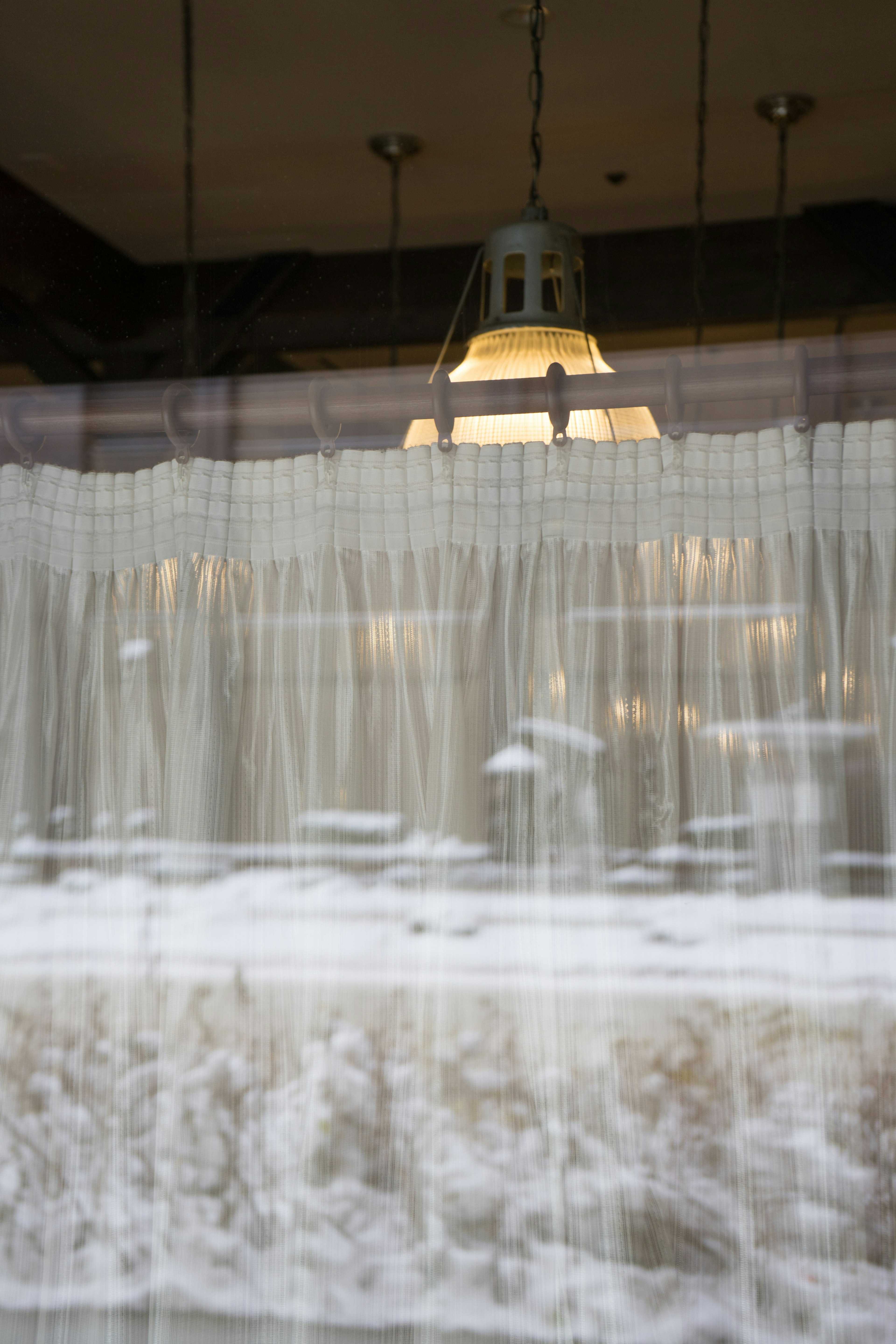 Bright lamp visible through sheer curtain with blurred scenery