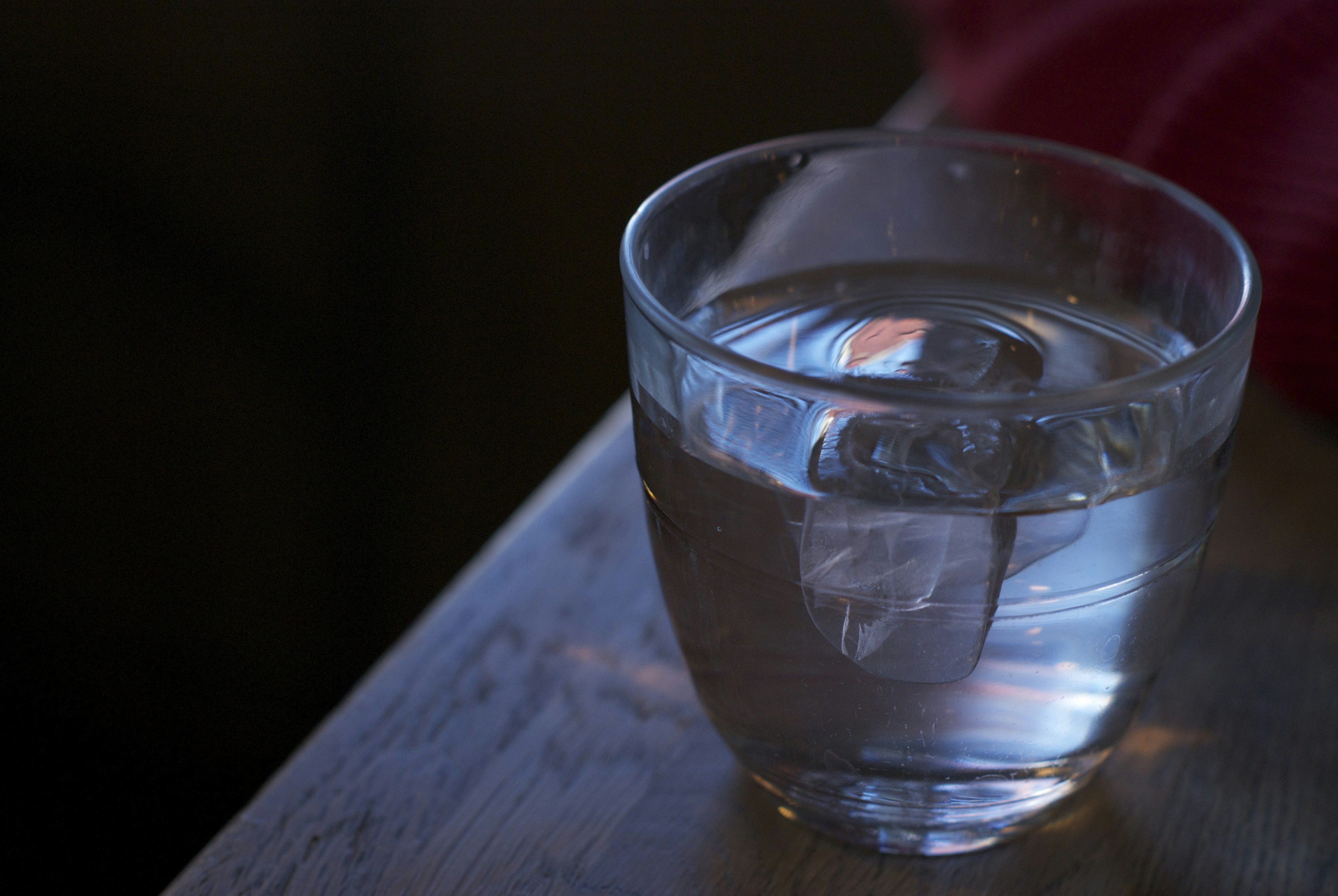 A clear glass of water with ice cubes sits on a wooden table