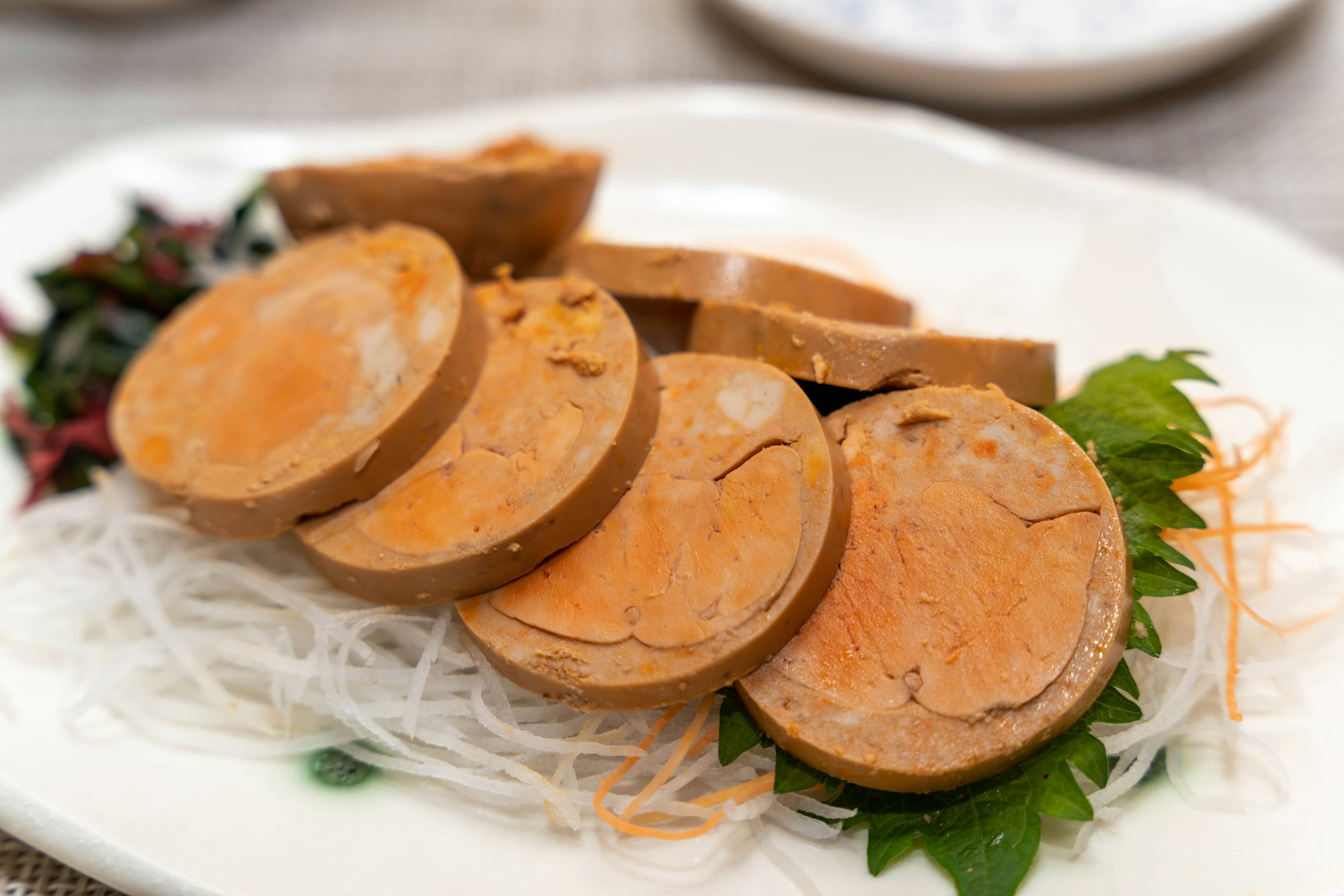 Sliced vegetarian sausage arranged on a plate with thin white noodles and green leaves