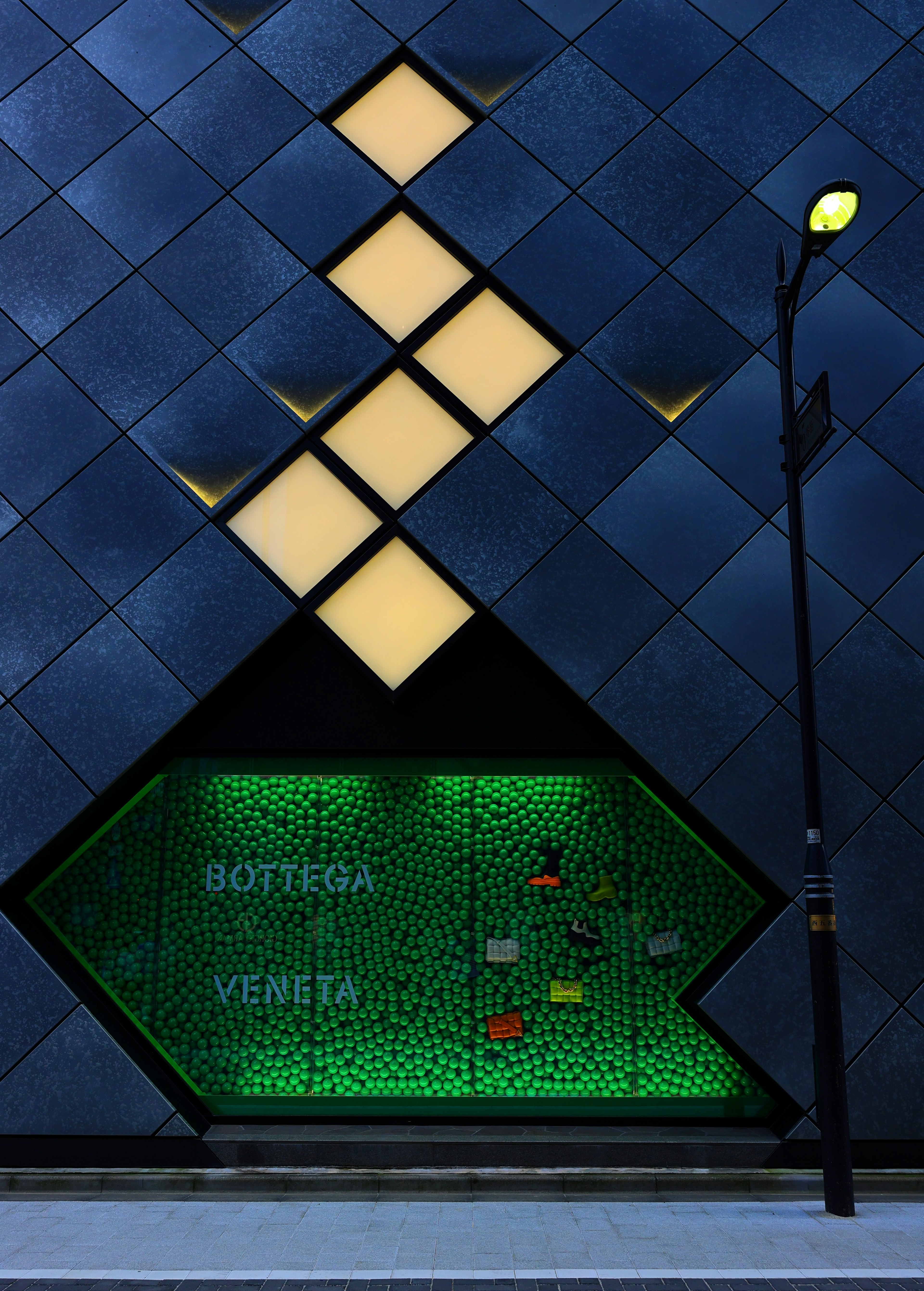 Blue exterior wall with diamond-shaped windows featuring a green display that reads Bottega Veneta