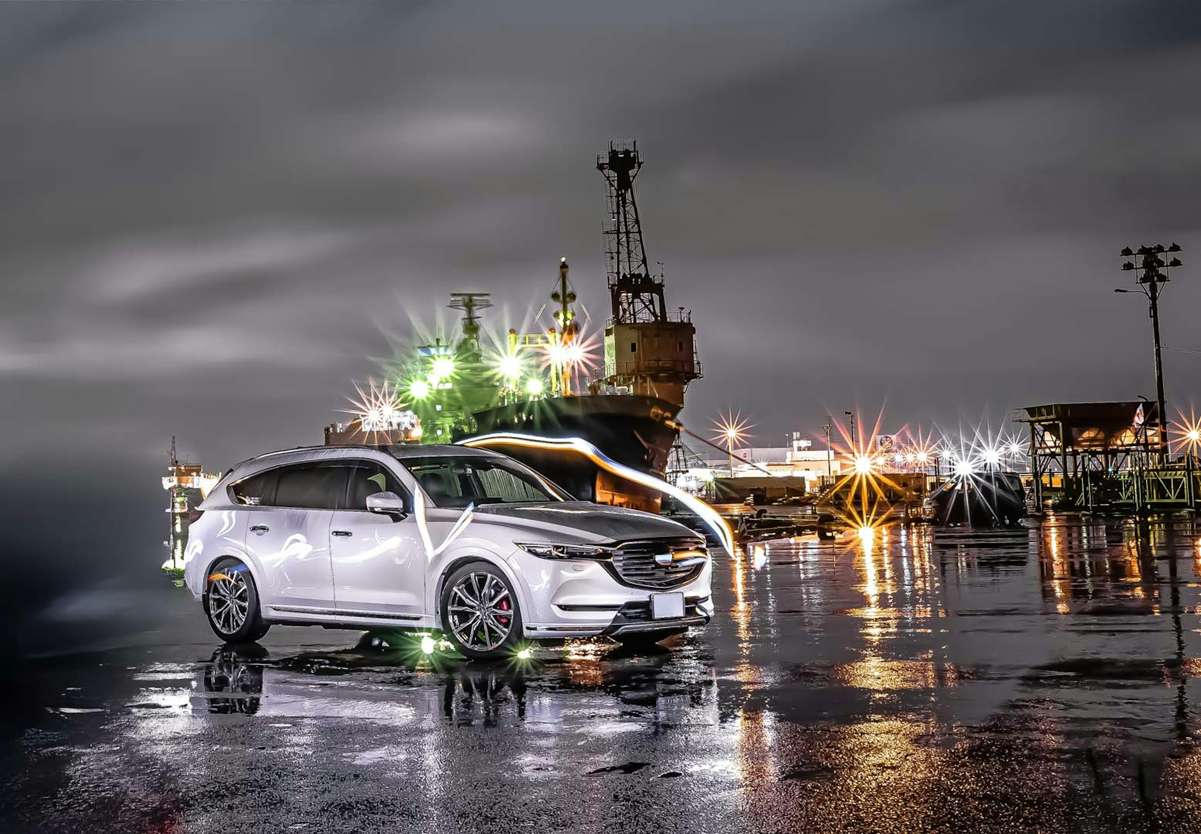 A white car parked at a harbor with a ship in the background at night