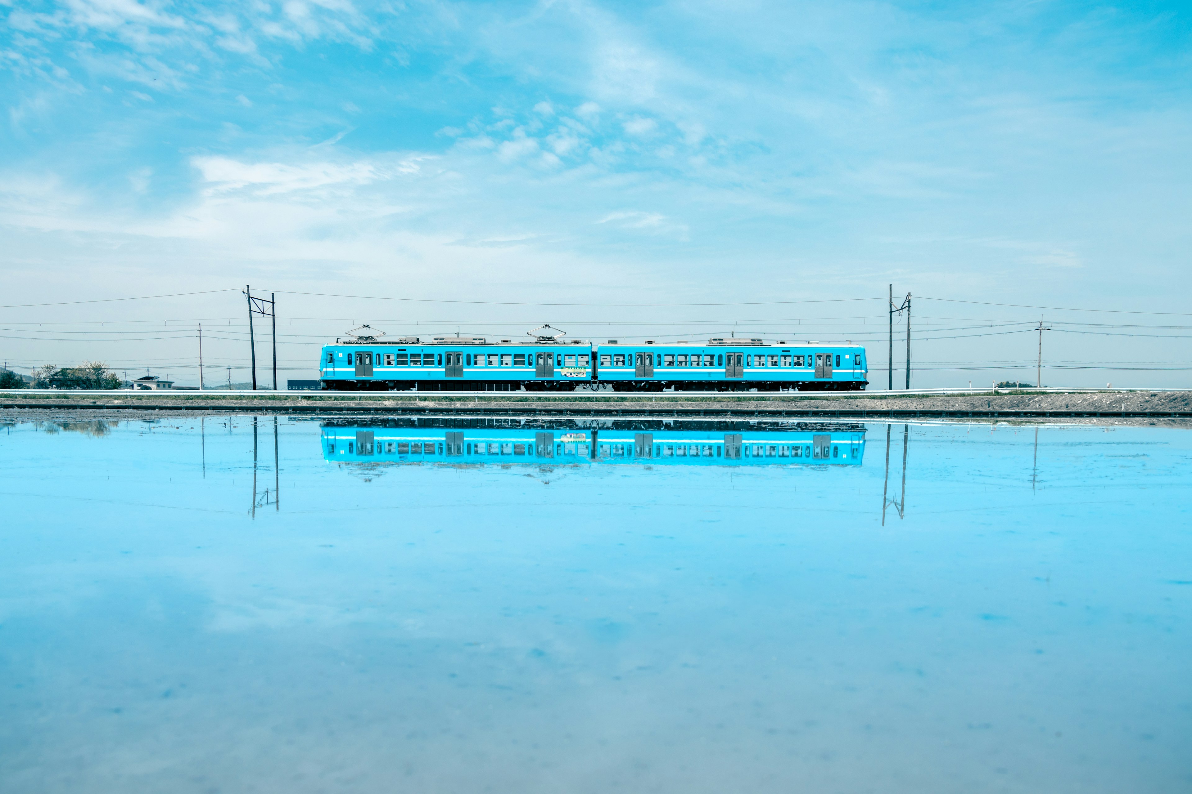 A blue train reflected in the water with a clear sky