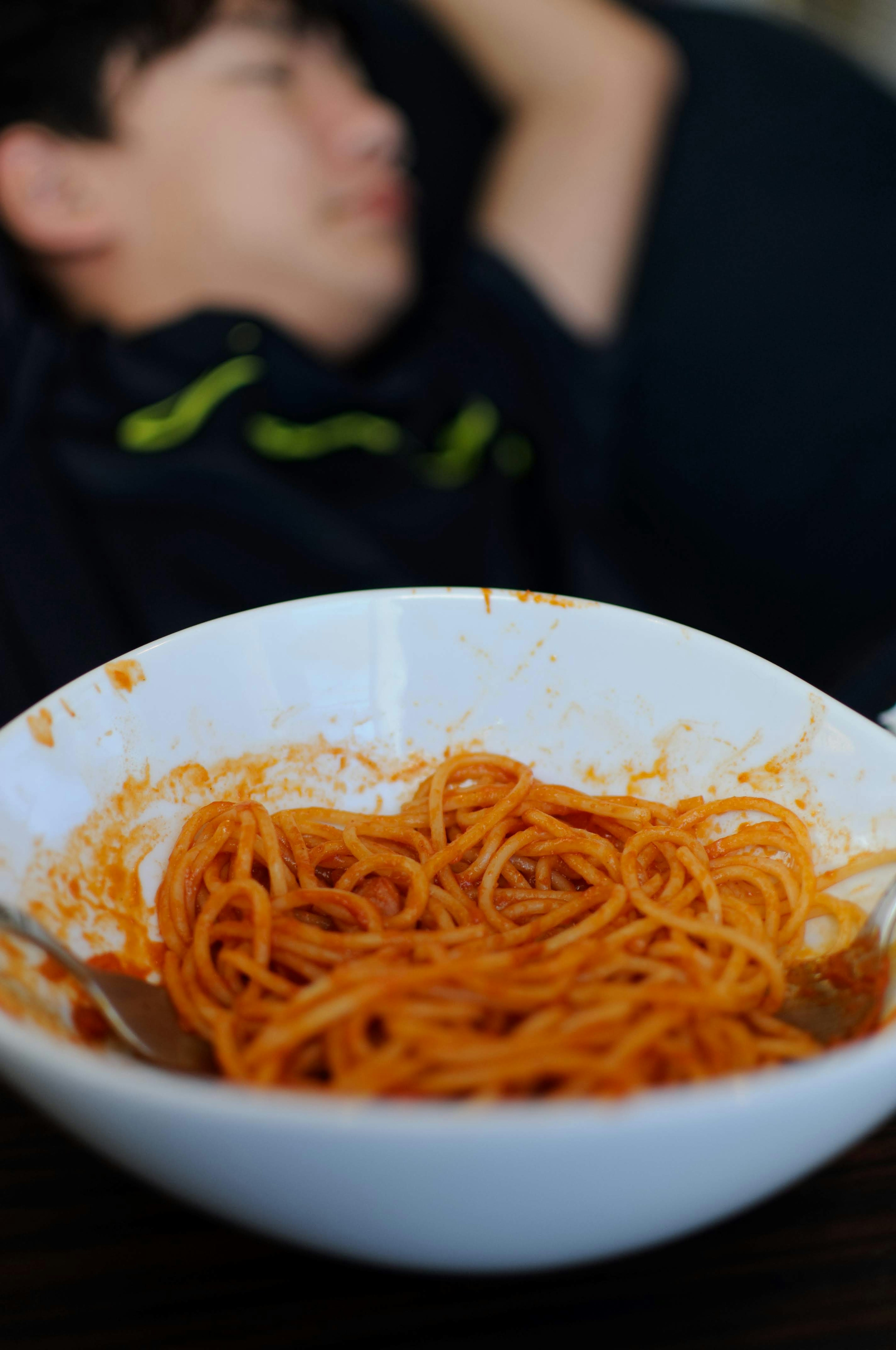 A white bowl of spaghetti with a blurred figure in the background