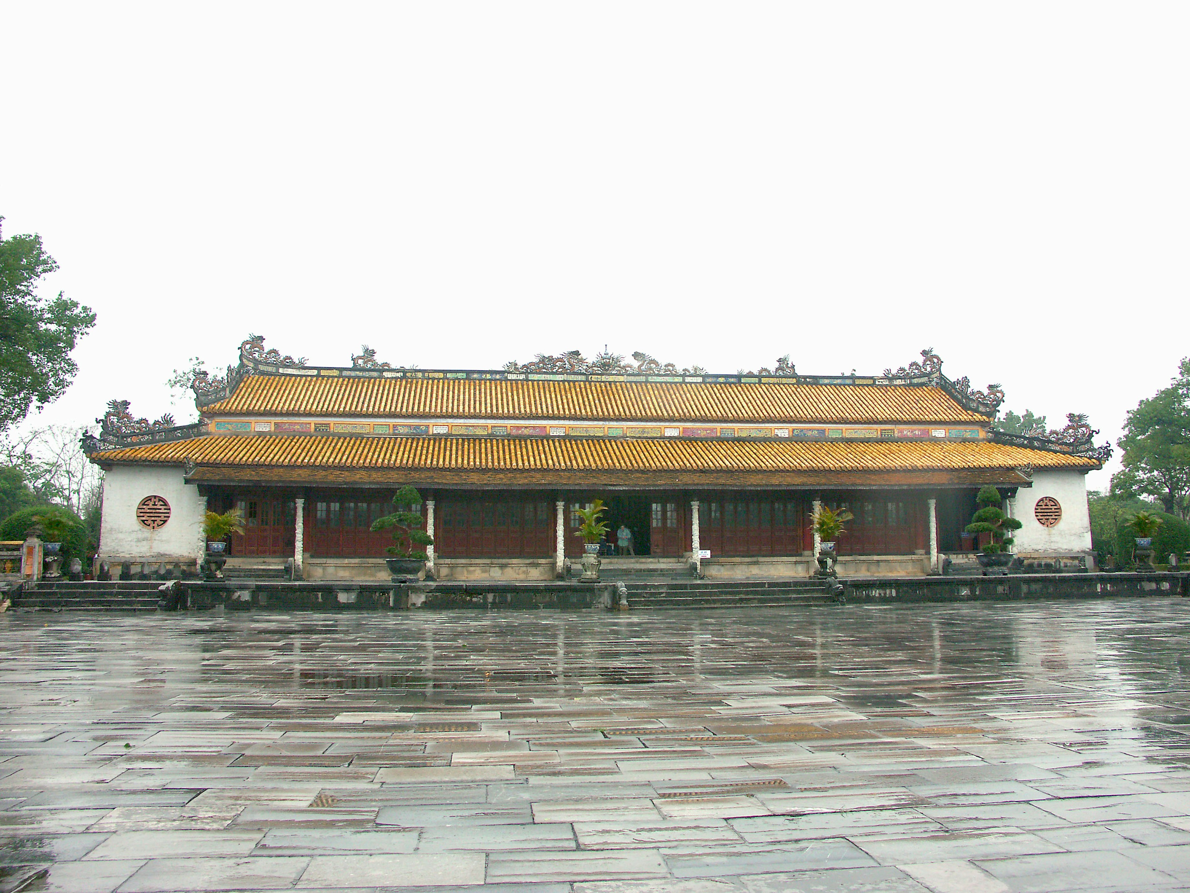 Ancient palace structure with a golden roof on a rainy stone pavement