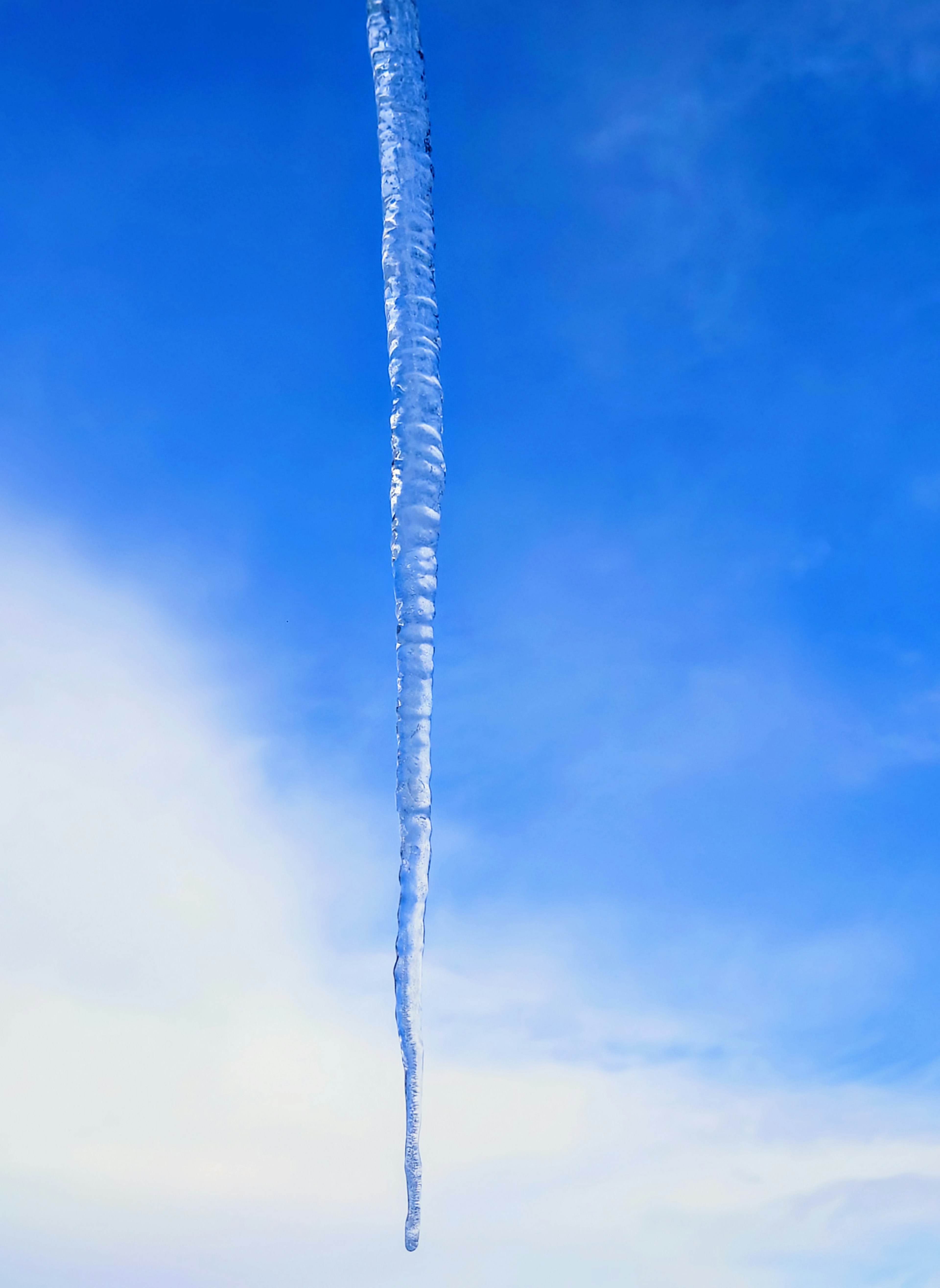 Vertical icicle hanging against a clear blue sky