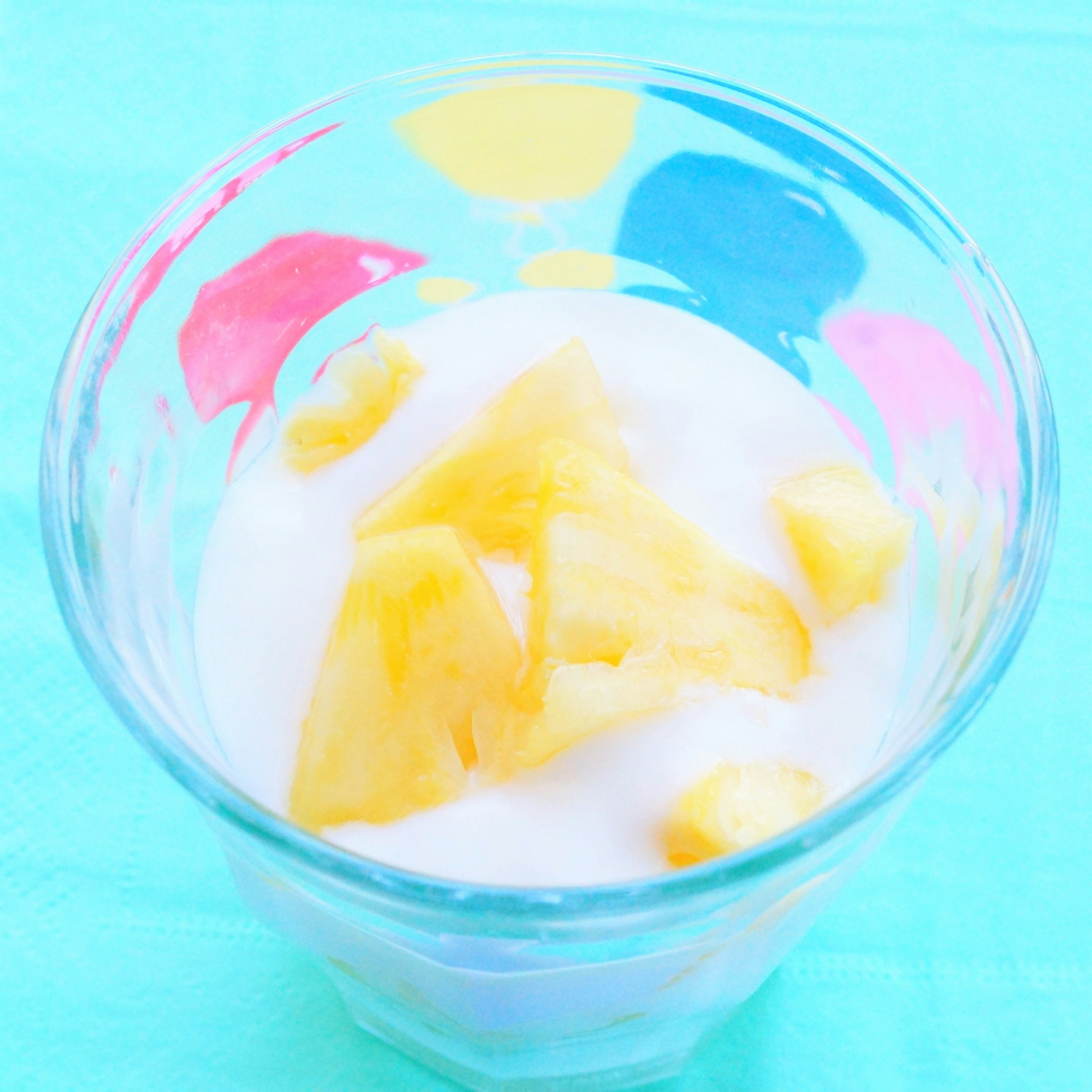 Bicchiere colorato pieno di yogurt guarnito con pezzi di ananas