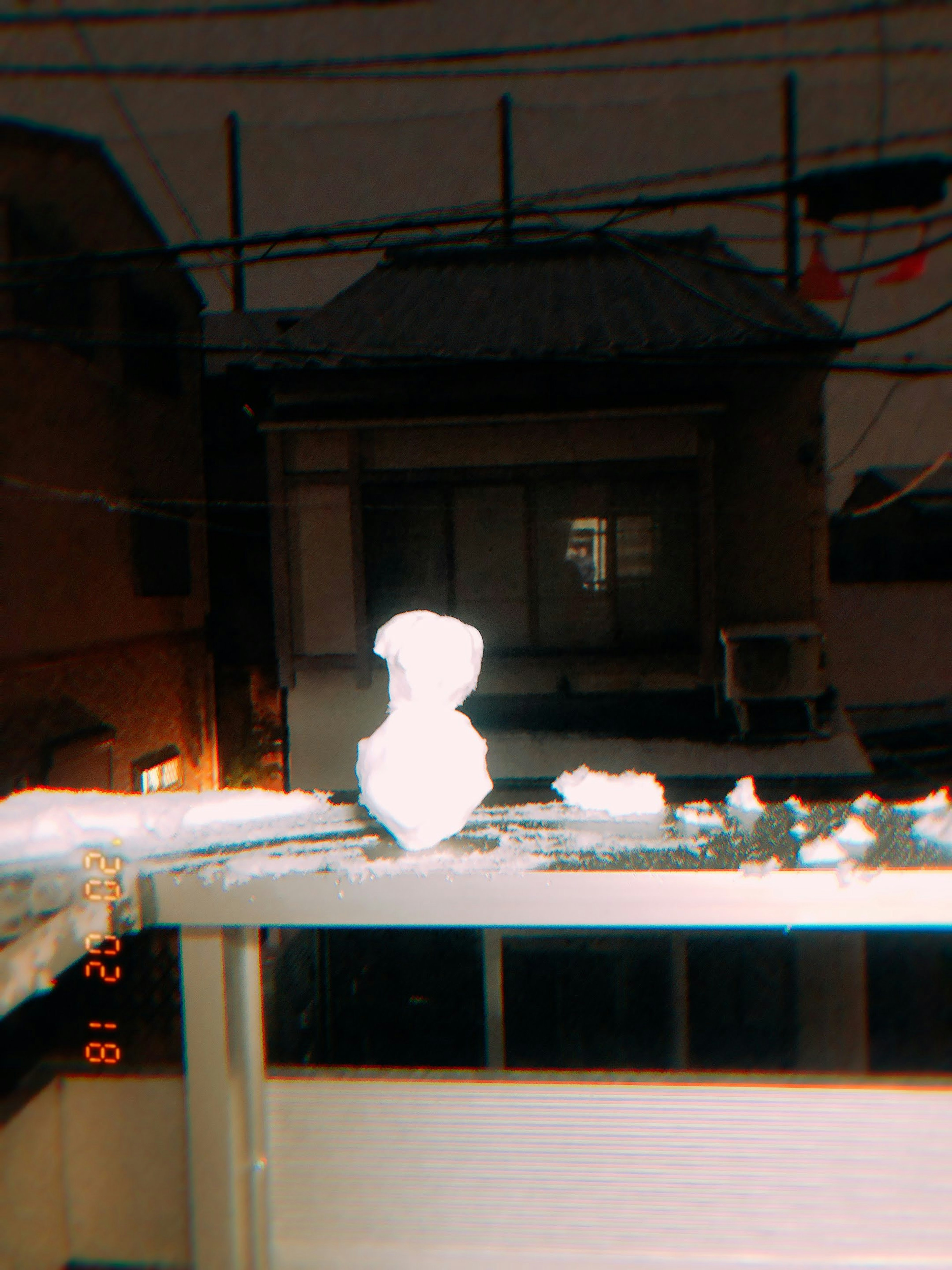 Snowman placed on a balcony with a house in the background