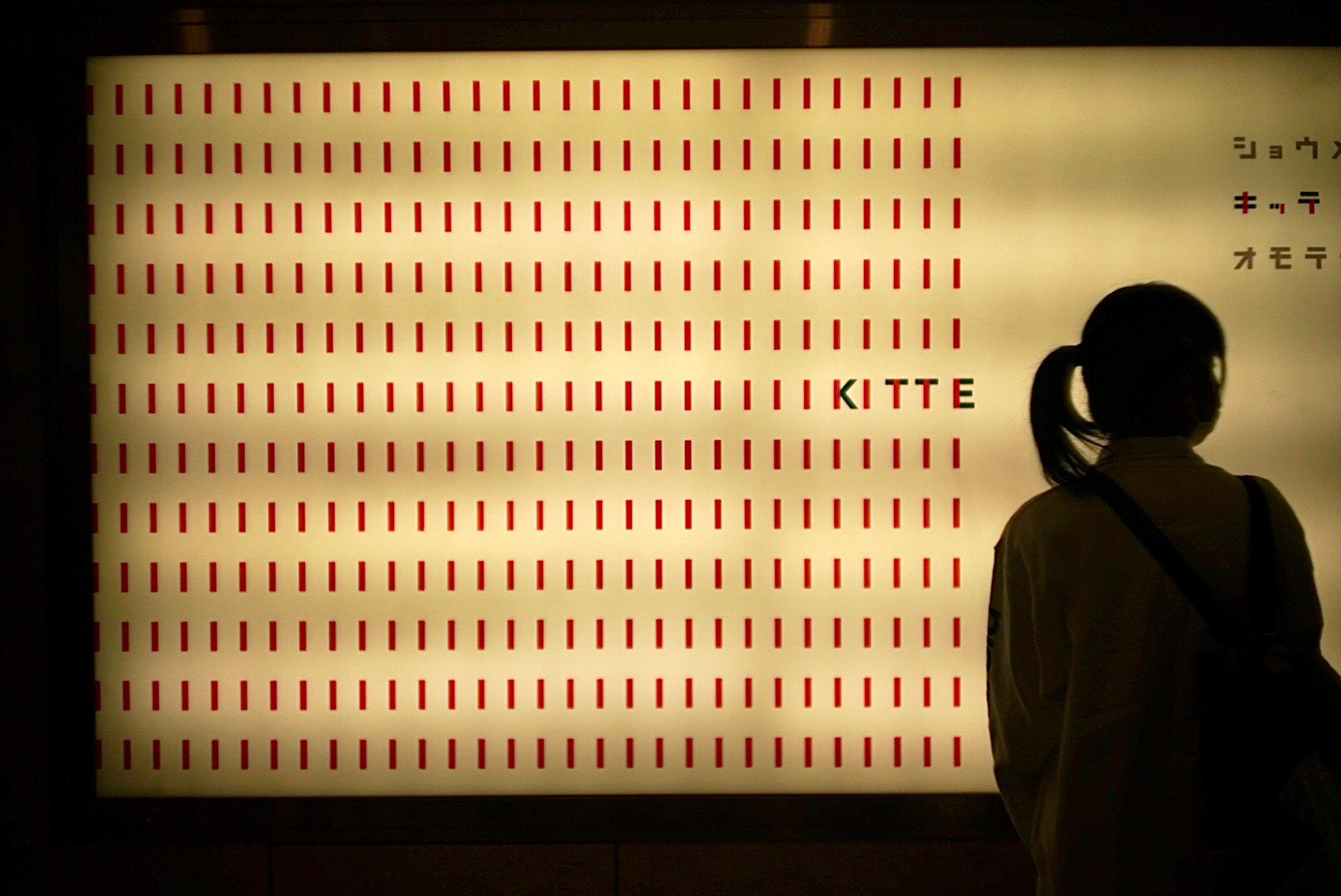 Silhouette d'une personne devant un mur couvert de lignes rouges et du mot KITTE