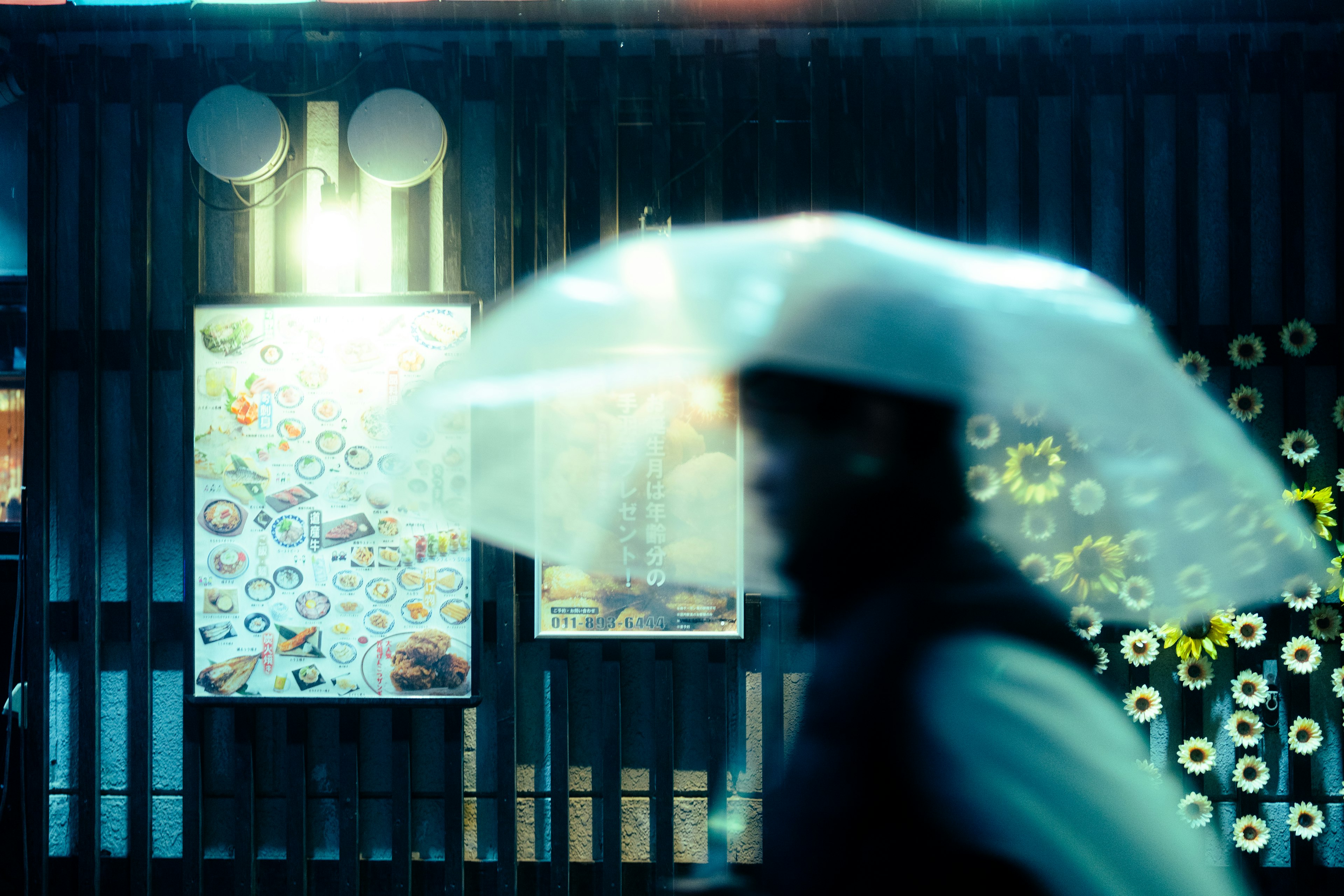 Persona caminando con un paraguas transparente bajo la lluvia con carteles coloridos al fondo