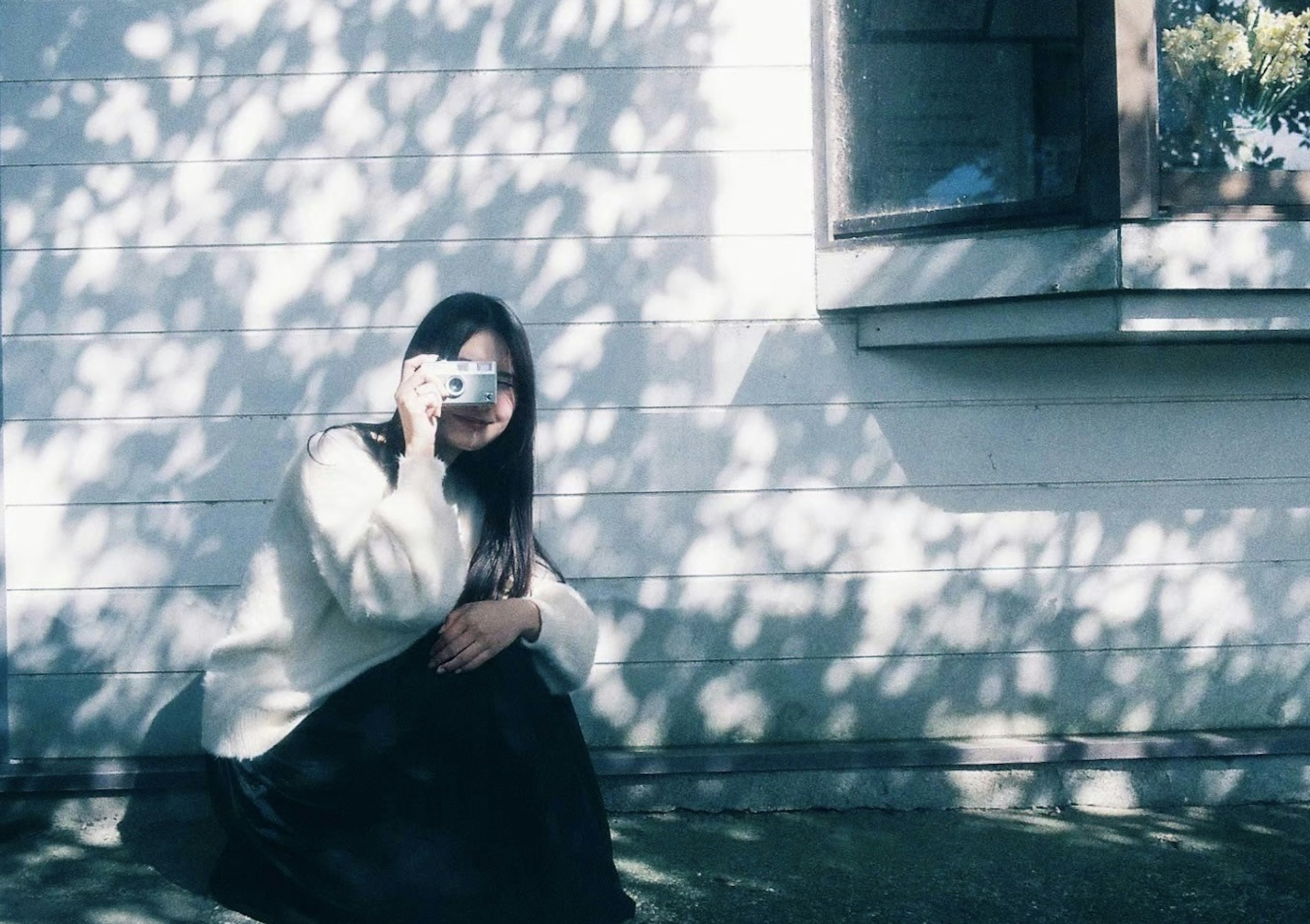 A woman sitting with a camera in a shadowy outdoor setting